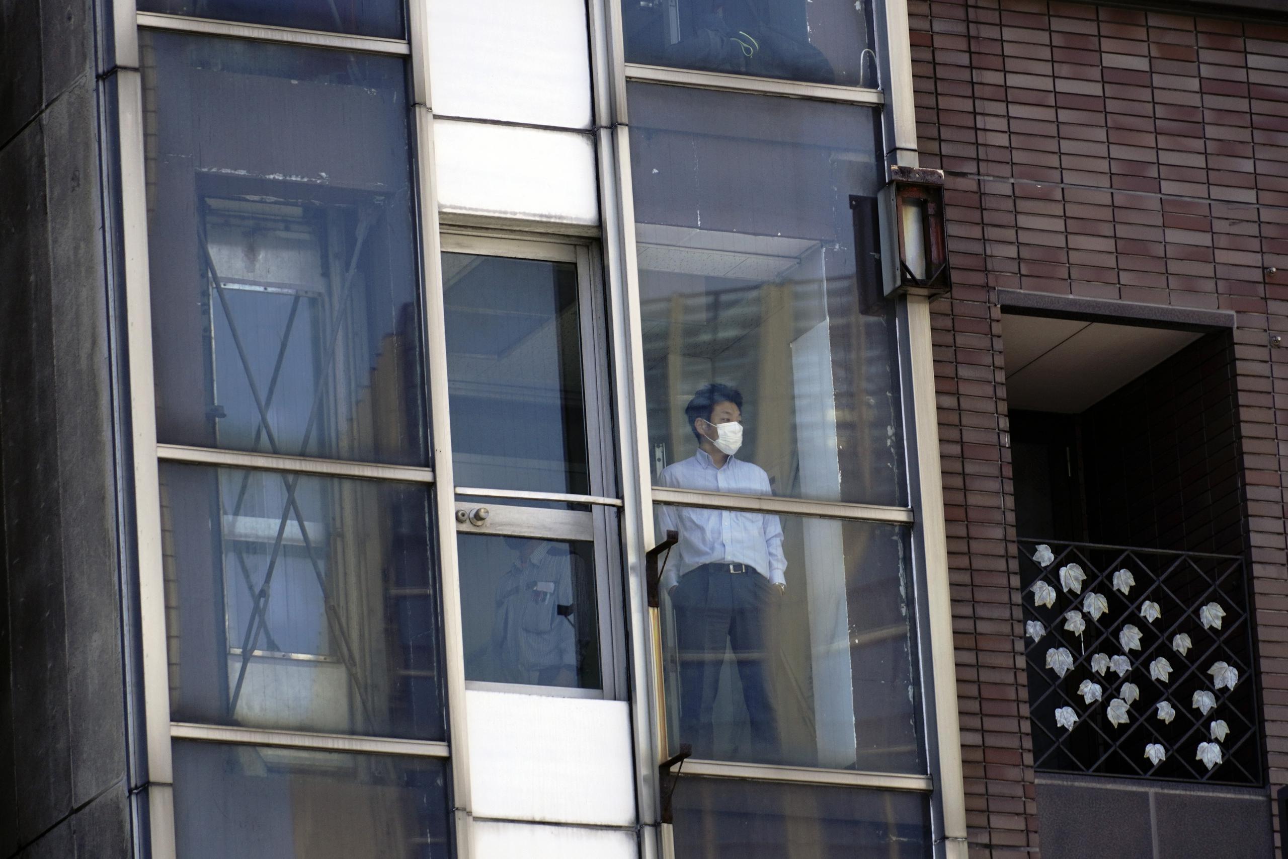 Un hombre con mascarilla para protegerse del coronavirus mira a través de la ventana de un edificio, en Tokio, el 14 de mayo de 2020.