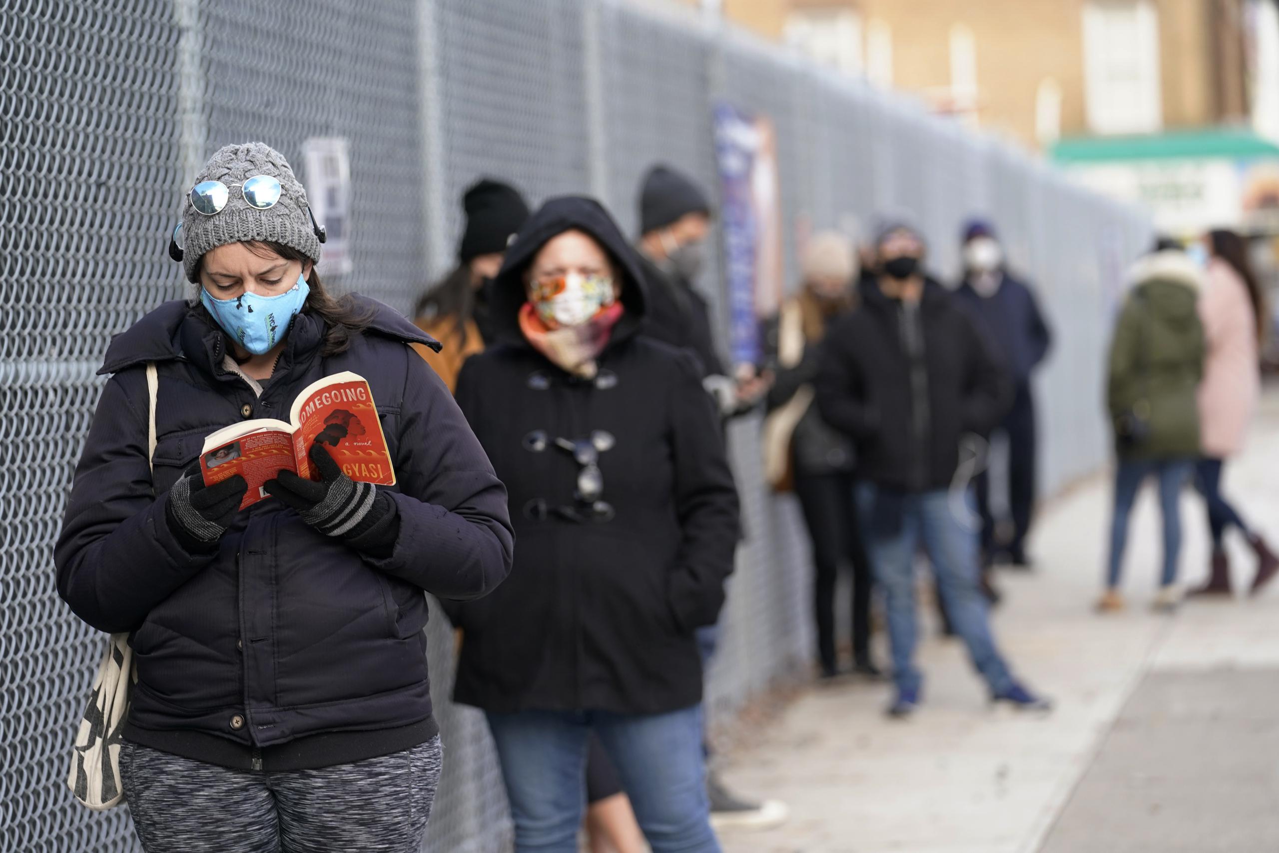 Ashley Gannon, izquierda, lee mientras espera en fila en las afueras de un sitio de pruebas de coronavirus en Brooklyn,  Nueva York.