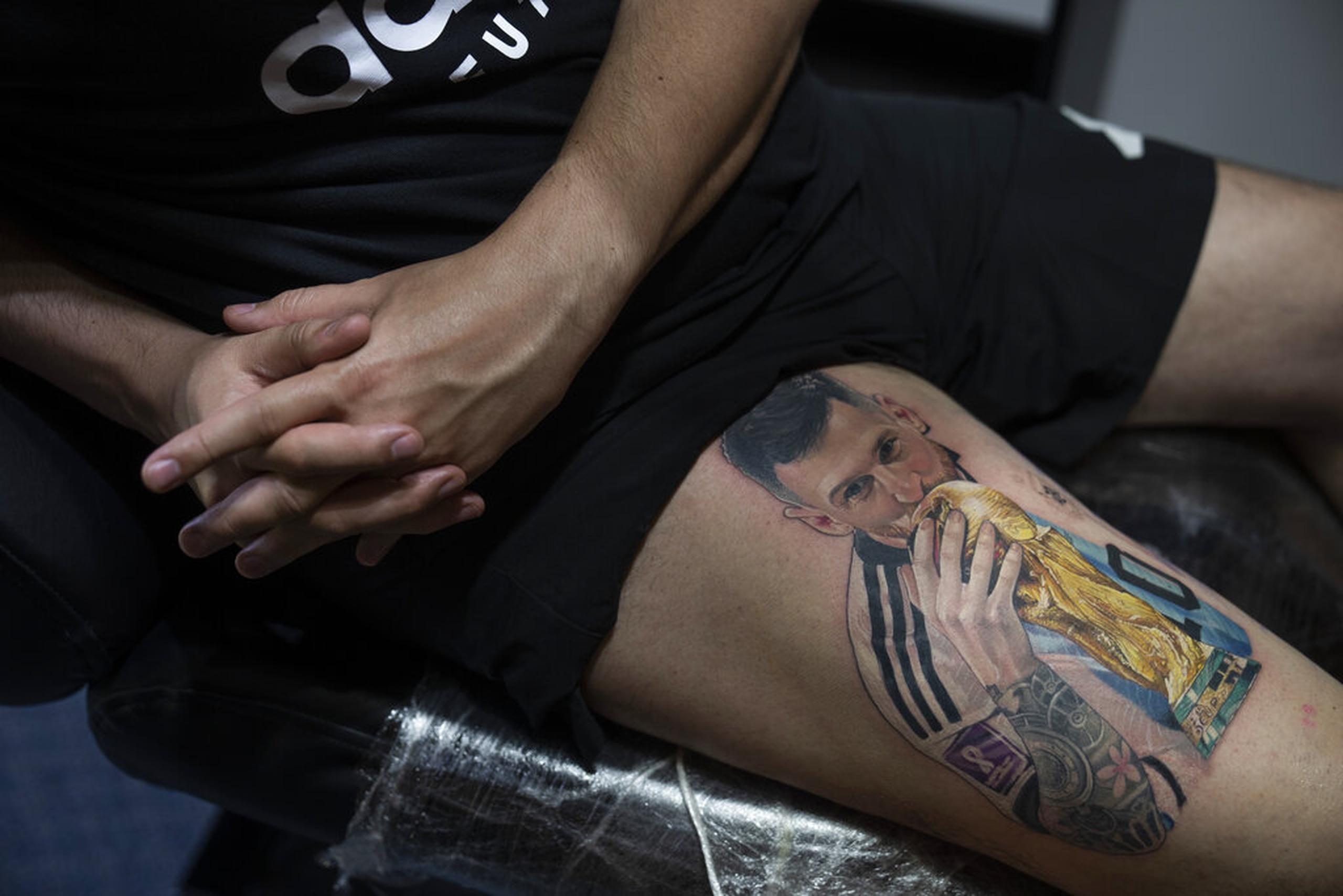 Sebastián Fernández descansa mientras el artista César "Yeyo" Molina le tatúa en la pierna una imagen del futbolista Lionel Messi besando la Copa del Mundo.