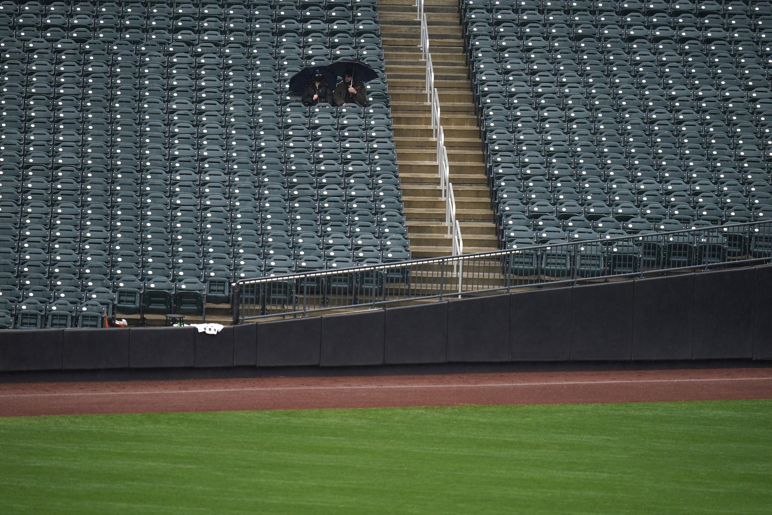 Fanáticos esperan bajo sombrillas el partido entre los Phillies y los Mets en Citi Field. Al final, el choque fue pospuesto.