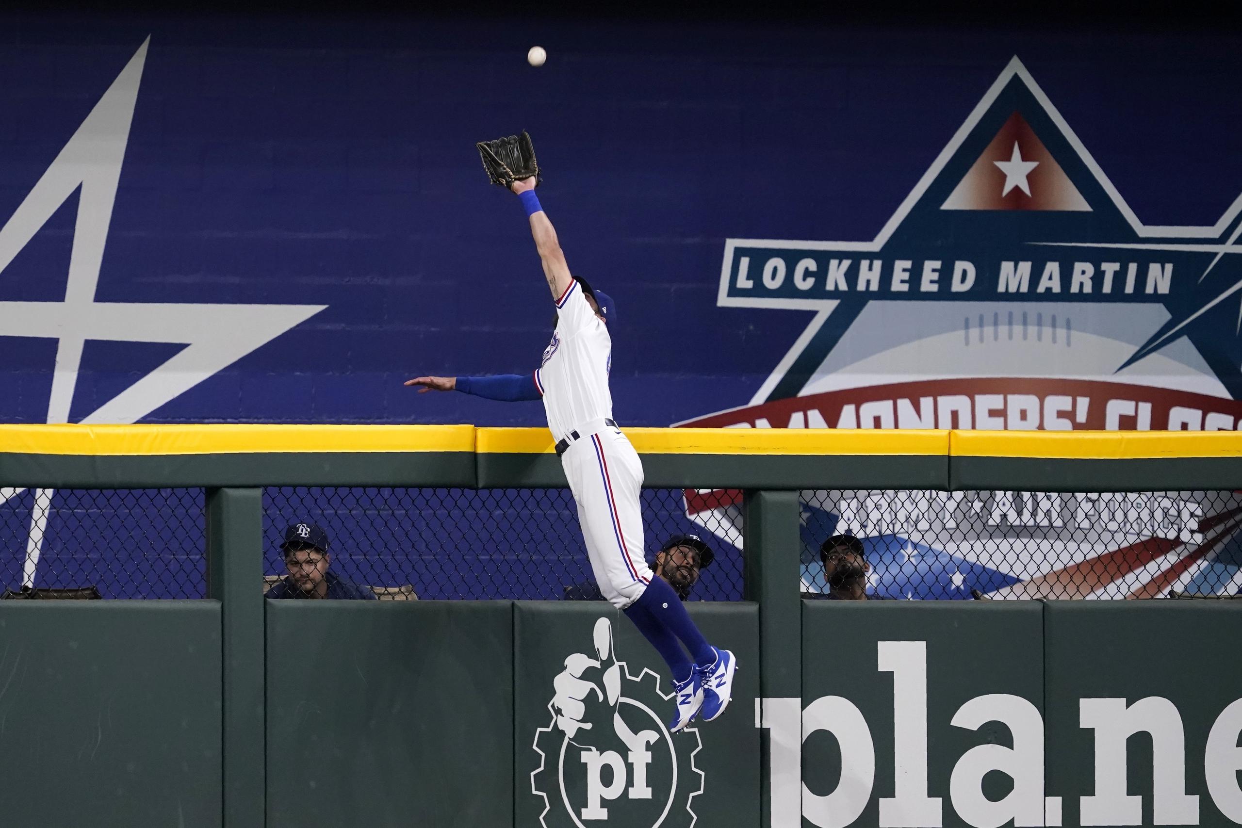 El jardinero central de los Rangers de Texas, Eli White, salta sobre el muro para atrapar un batazo de Ji-Man Choi, de los Rays de Tampa Bay, en el primer inning del juego de la MLB que enfrentó a ambos equipos el 30 de mayo de 2022, en Arlington, Texas.