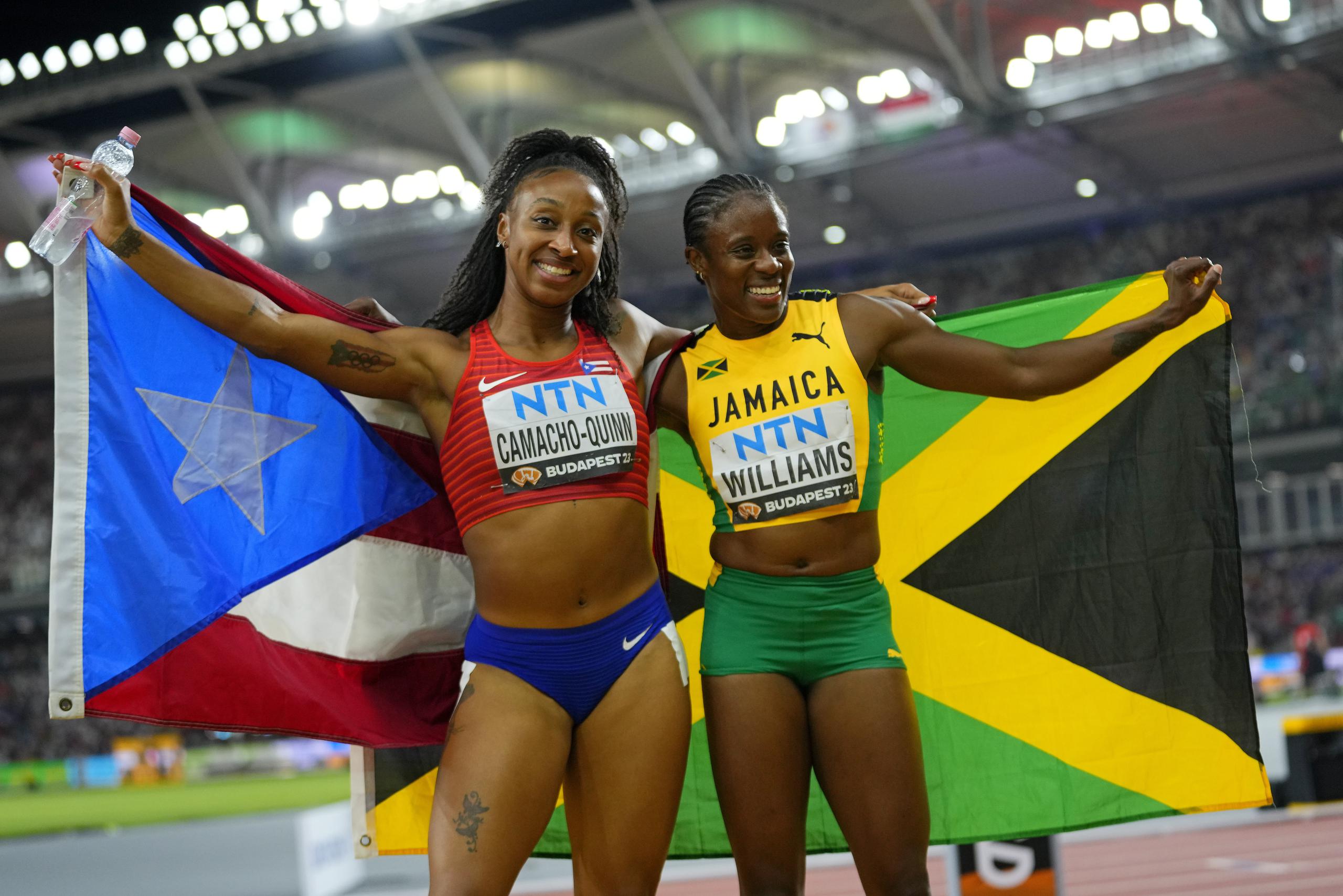 Jasmine Camacho Quinn y Danielle Williams, plata y oro en la final de los 100 metros con vallas, posan tras la carrera mostrando las banderas de sus respectivos países, Puerto Rico y Jamaica.