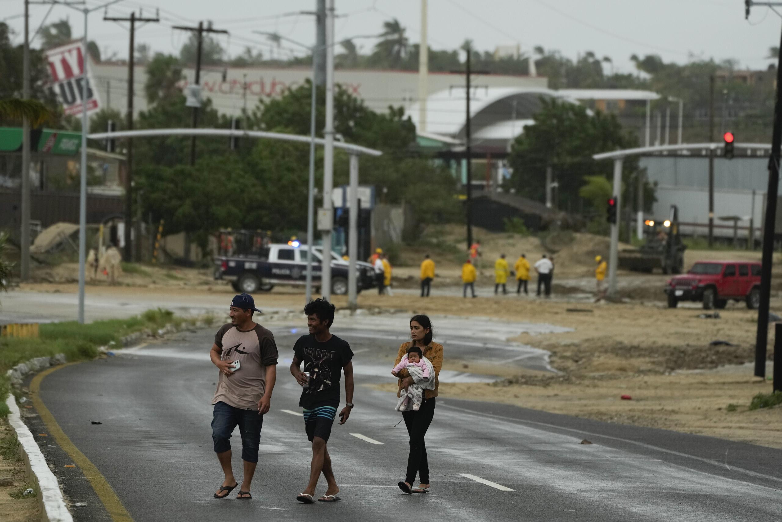 Residentes cruzan cerca de una avenida inundada por las lluvias generadas por el huracán Norma en San José del Cabo, México, el sábado 21 de octubre de 2023. (AP Foto/Fernando Llano)