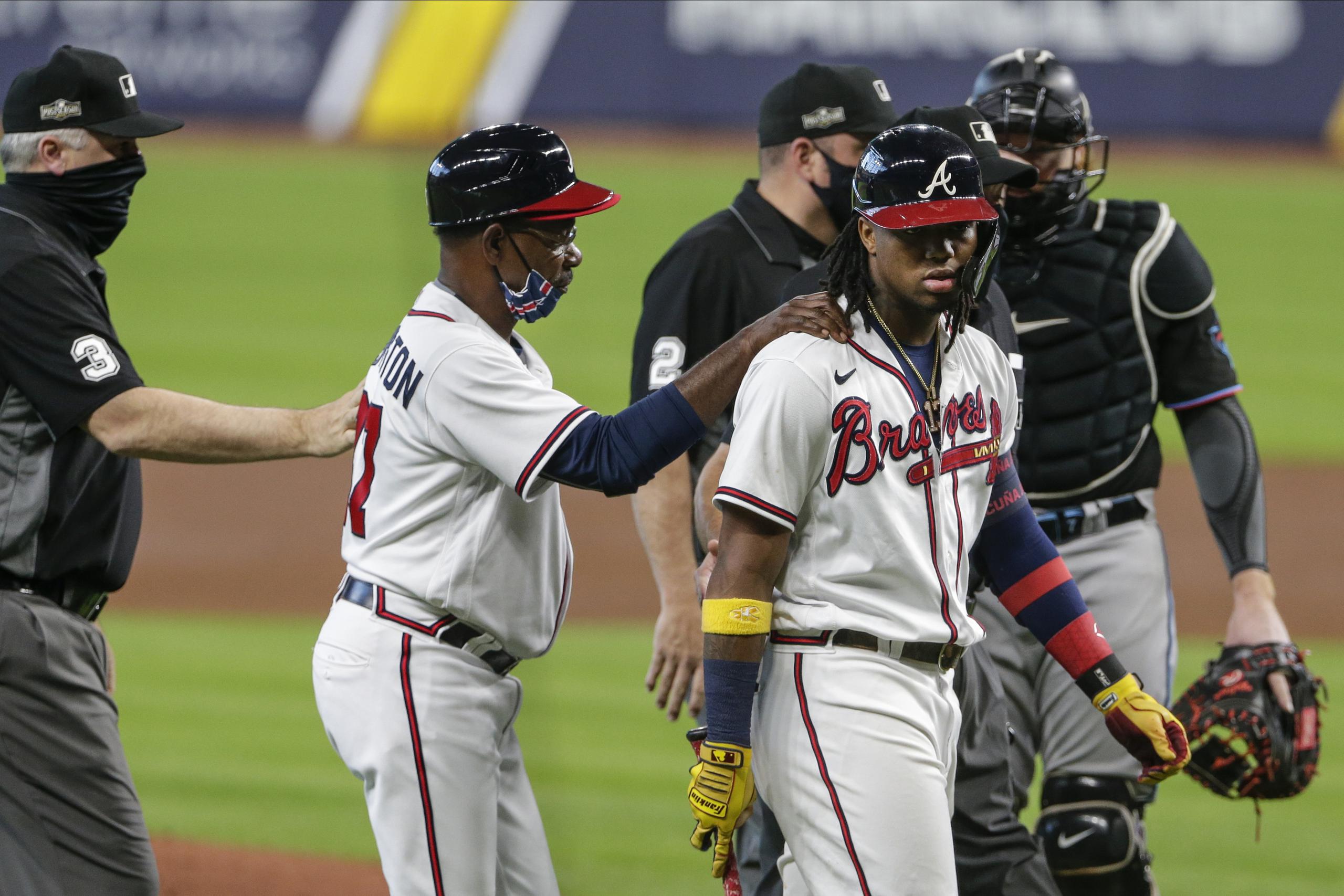 El coach de tercera base de los Braves de Atlanta Ron Washington consuela a Ronald Acuna Jr. después de recibir un pelotazo en la tercera entrada del primer juego de la Serie Divisional contra los Marlins.