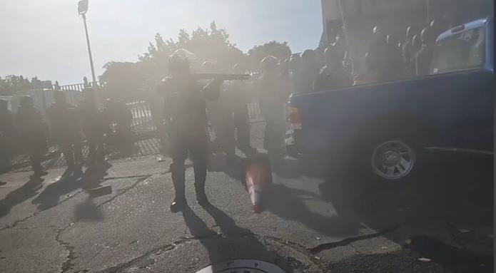 Momento en que un agente sostiene un arma contra los manifestantes y que fue captado por una vecina del lugar.