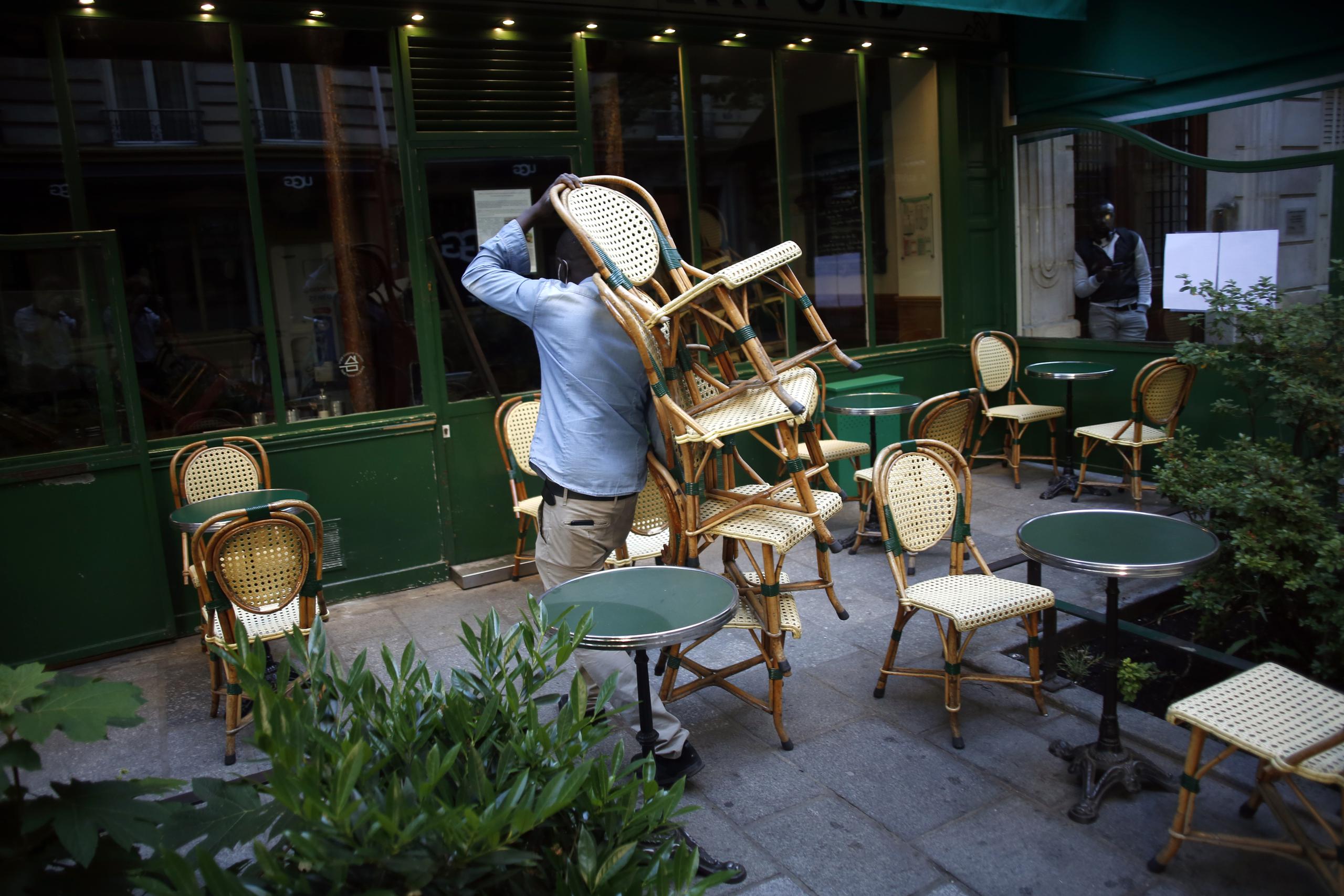 Un empleado acomoda las sillas para cumplir con el distanciamiento social en los restaurantes de París.