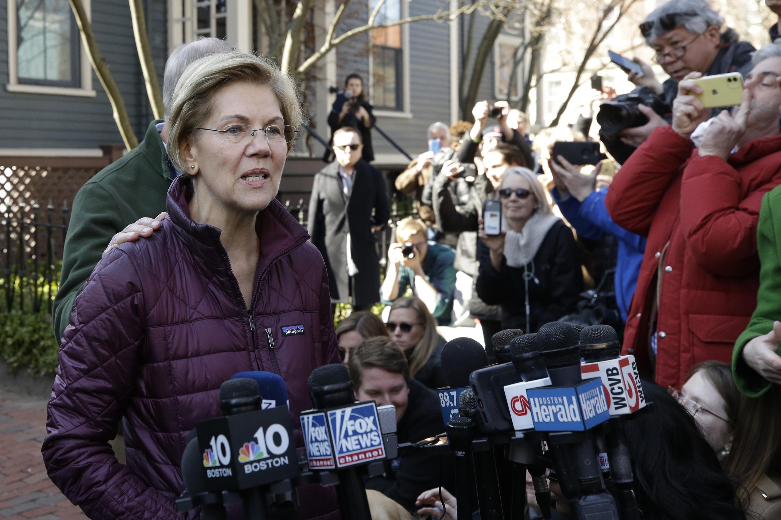 Elizabeth Warren, acompañada por su esposo Bruce Mann, habla con la prensa frente a su casa en Cambridge, Massachusetts, tras anunciar su retiro de la contienda presidencial