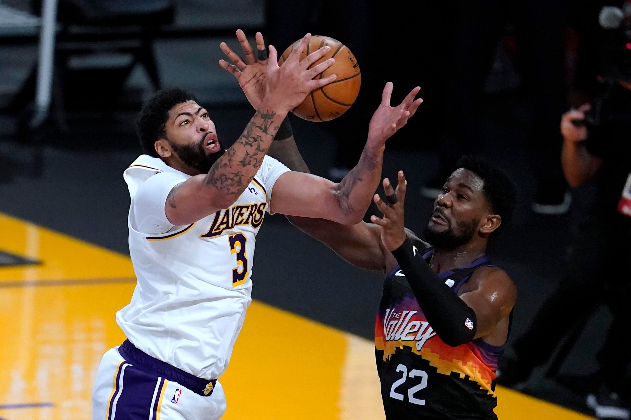 El alero de los Lakers Anthony Davis (3) lucha un rebote ante el centro de los Suns Deandre Ayton.