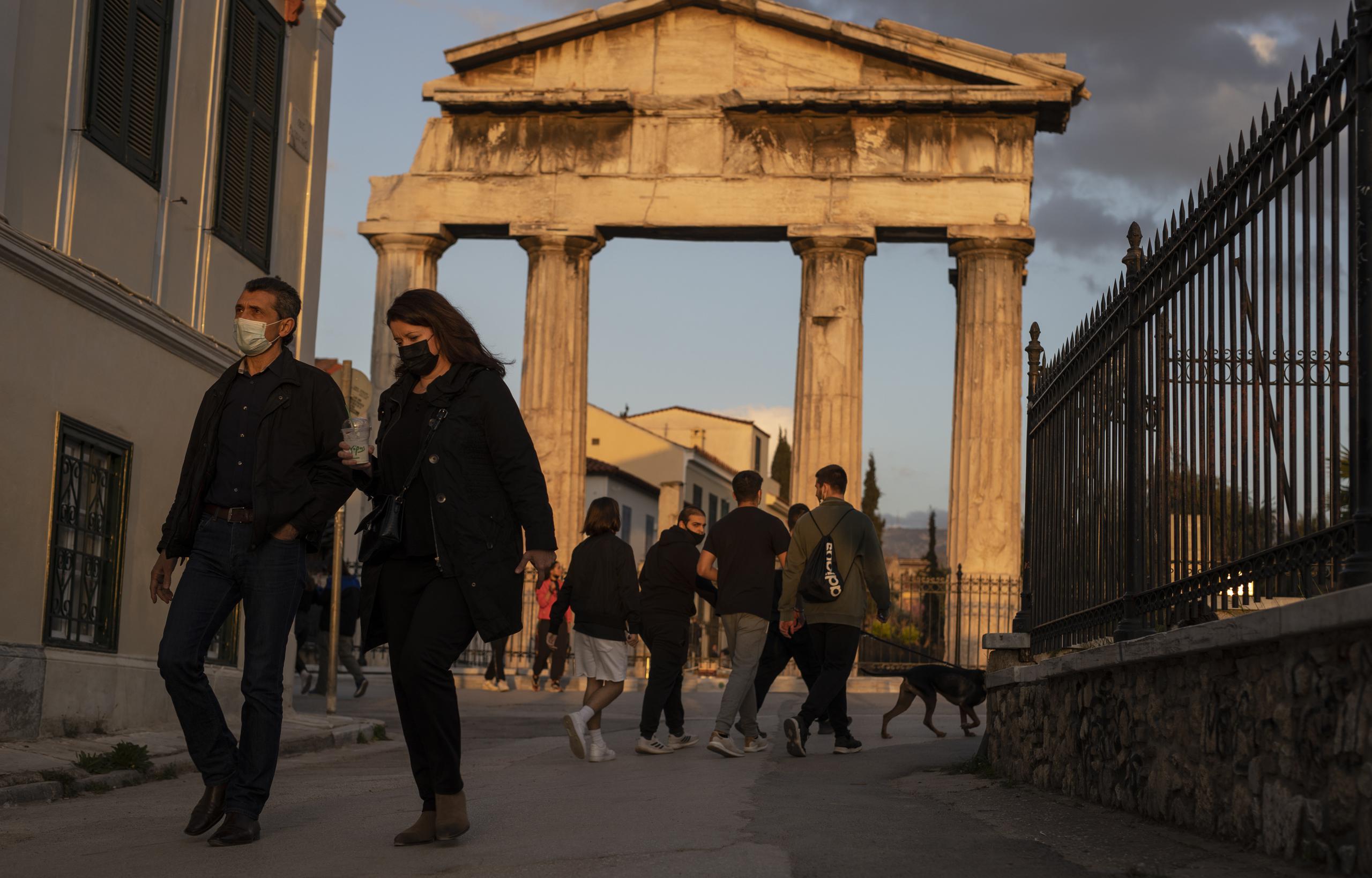 Personas con mascarillas caminan frente a la puerta del antiguo ágora romano, en Plaka, un distrito de Atenas, el martes 6 de abril de 2021.