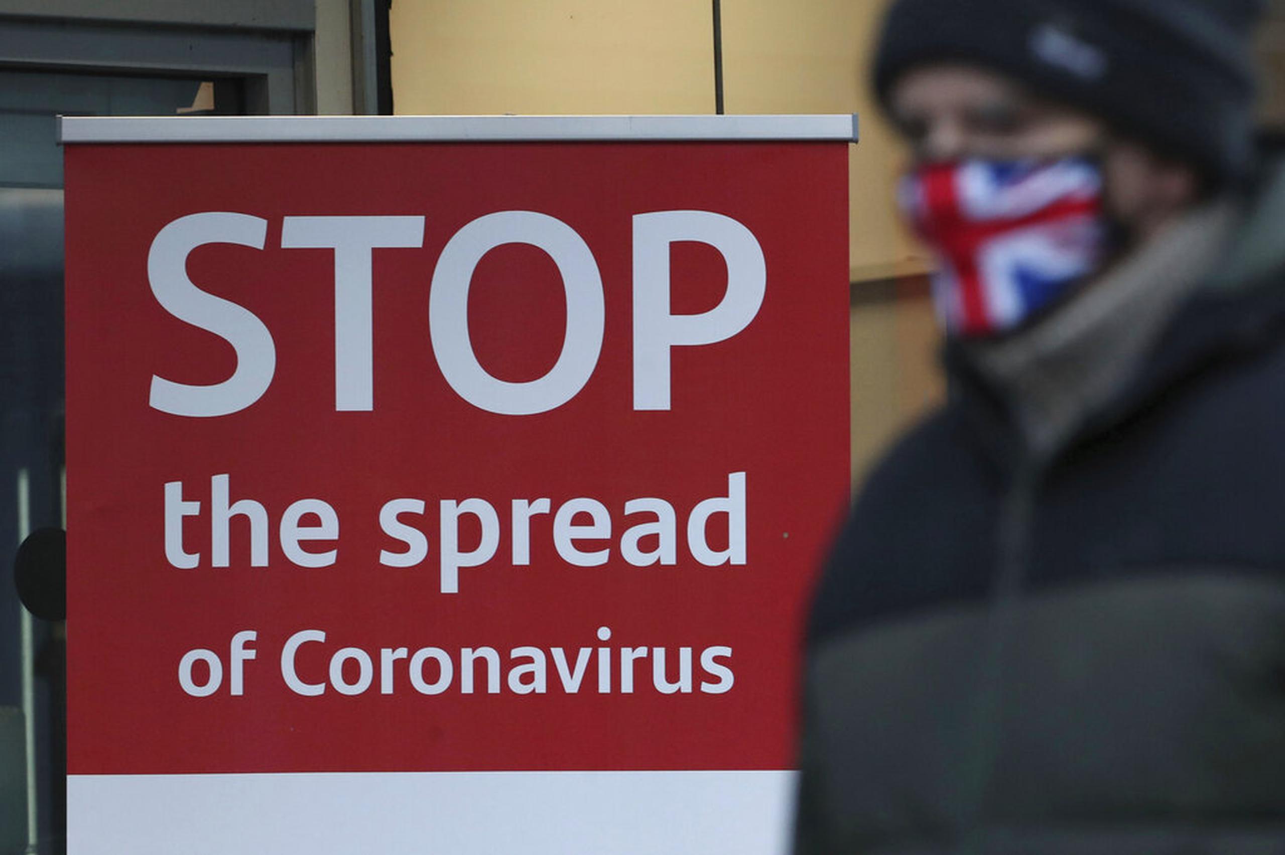Una persona pasa frentea a un letrero que pide frenar la diseminación del coronavirus afuera de un banco en Glasgow, Escocia.