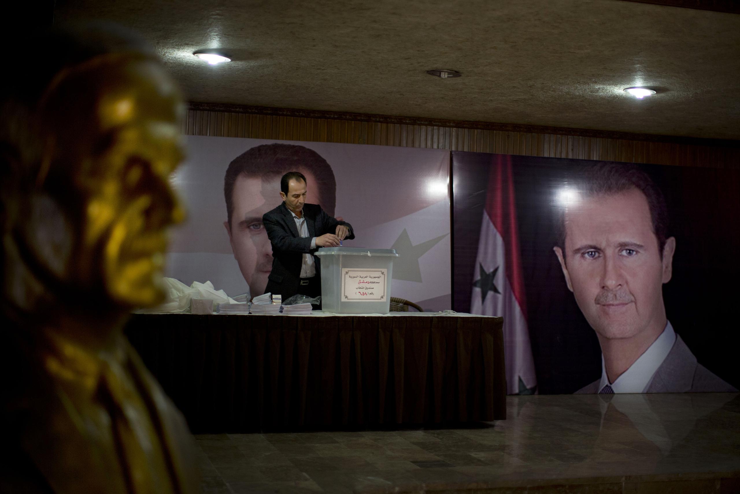 Un funcionario sirio espera en abril de 2016 a los votantes en un centro electoral, junto a carteles del presidente, Bashar Assad, durante las elecciones parlamentarias en Damasco, Siria.