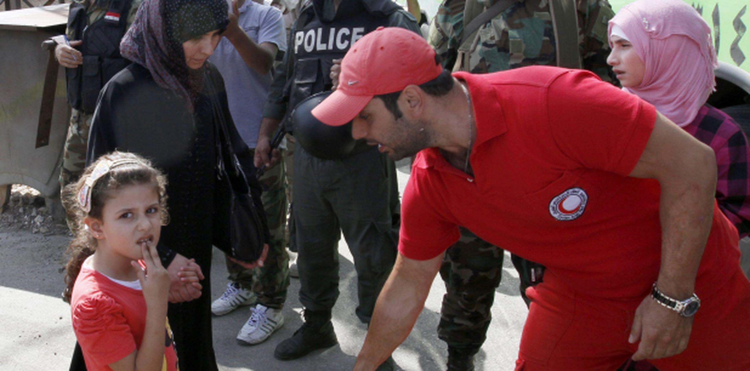 Un voluntario de la Media Luna roja ayuda a una niña siria y a algunas mujeres. (EFE)