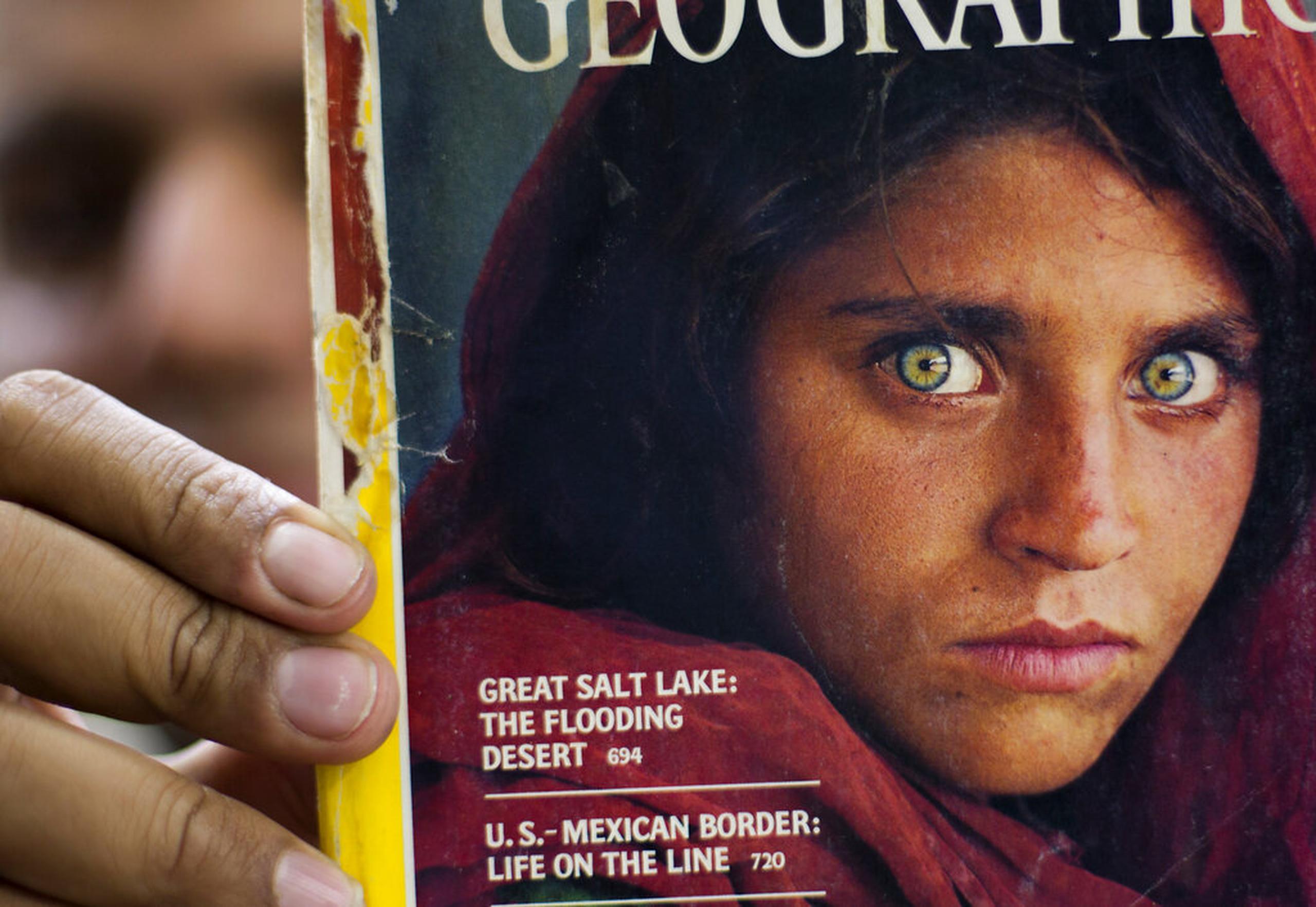 En esta foto del 26 de octubre de 2016, el paquistaní Inam Khan, dueño de una librería, muestra una copia de la revista de National Geographic con la imagen de la refugiada afgana Sharbat Gulla, en Islamabad, Pakistán.