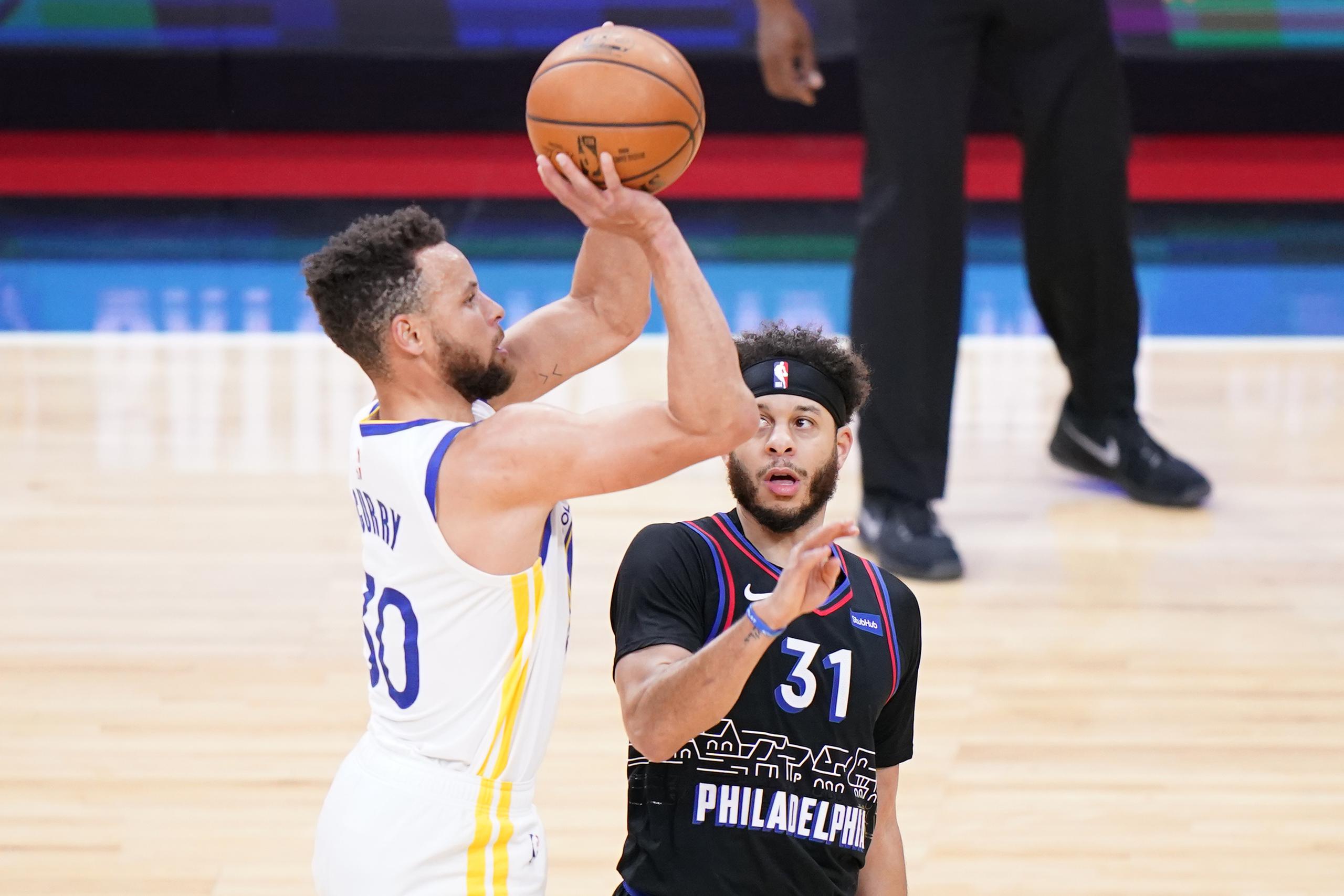 Stephen Curry, de los Warriors de Golden State, se levanta para tirar mientras lo observa su hermano Seth Curry, de los Sixers de Filadelfia.