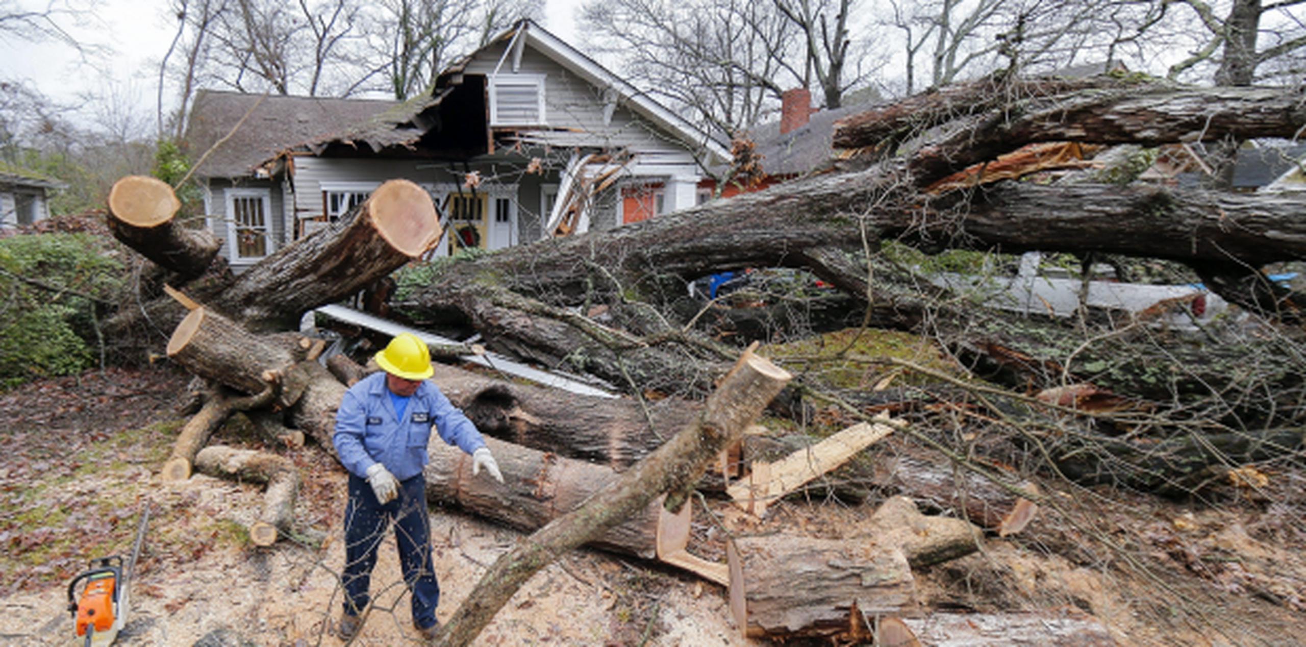 Un operario corta un árbol que cayó sobre una casa y varios coches durante las tormentas que afectaron a la ciudad de East Point, Georgia, (Agencia EFE)