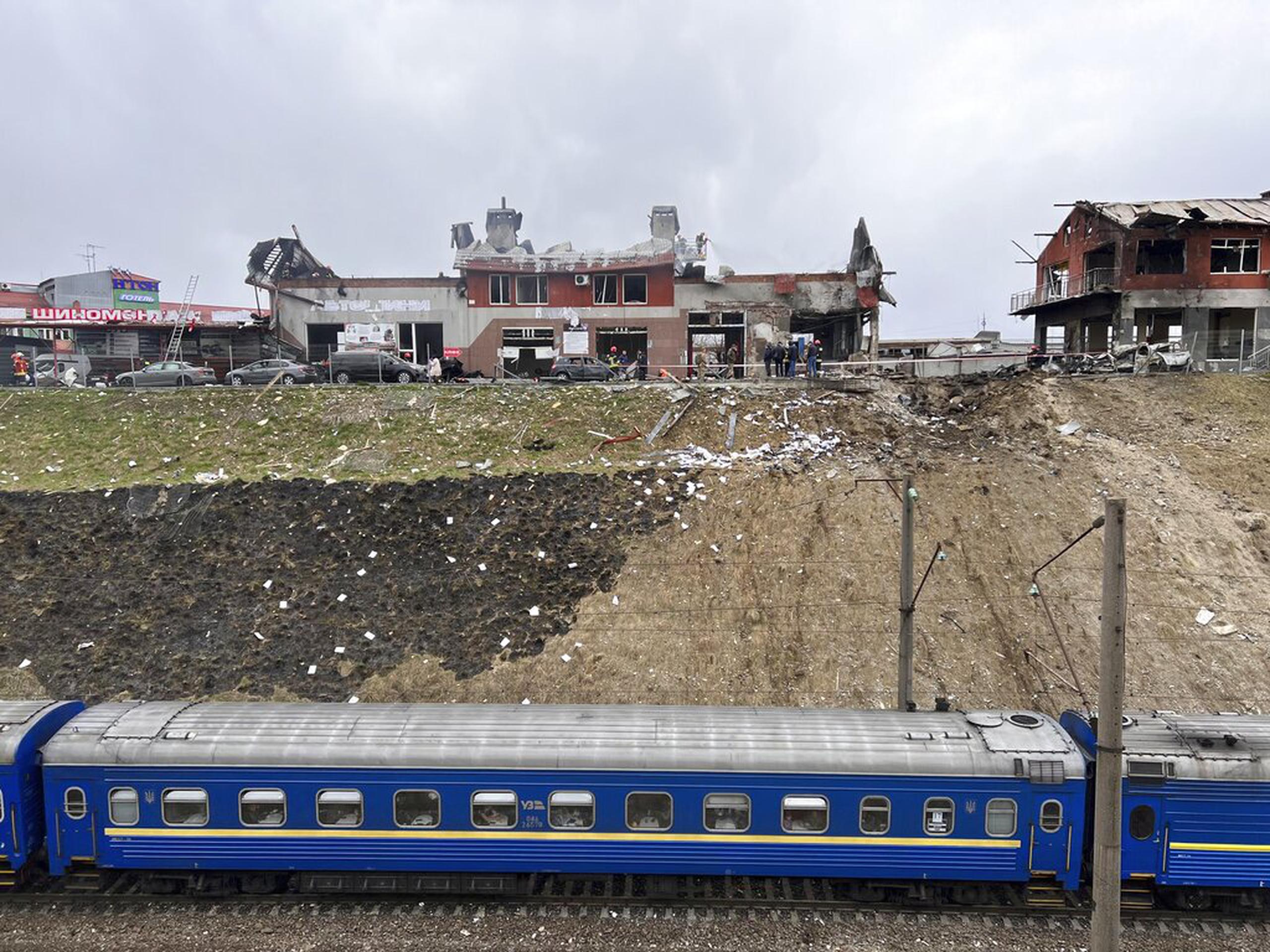 Un tren que viaja desde Dnipro pasa por el área donde personal de emergencia limpia los escombros después de un ataque aéreo en un establecimiento de neumáticos en la ciudad occidental de Leópolis, Ucrania, el 18 de abril de 2022.