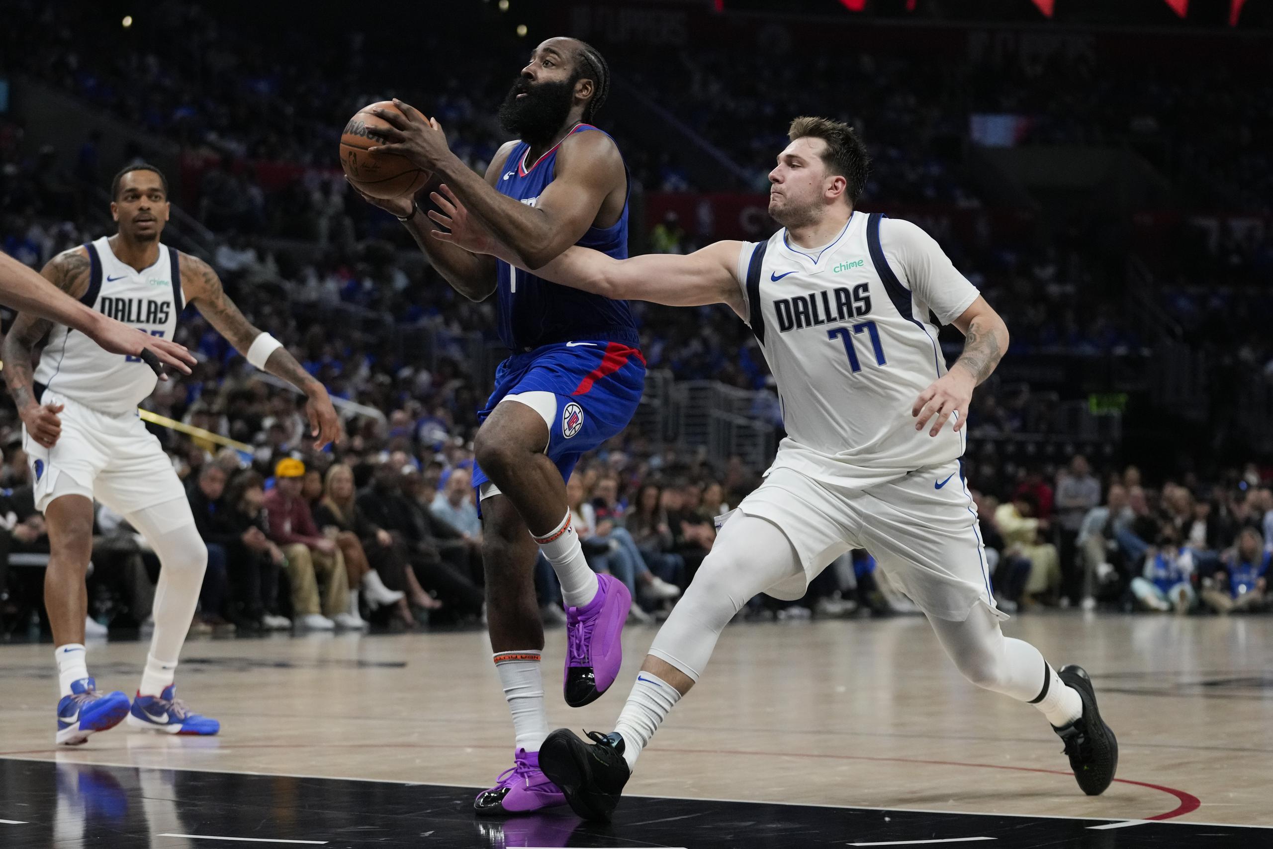 Luka Doncic (77), de los Mavericks de Dallas, intenta defender una canasta de James Harden (1), de los Clippers de Los Ángeles, durante la primera mitad del Juego 1 de la serie de playoffs de primera ronda de baloncesto de la NBA, en Los Ángeles, el domingo 21 de abril de 2024. (AP Foto/Ashley Landis)