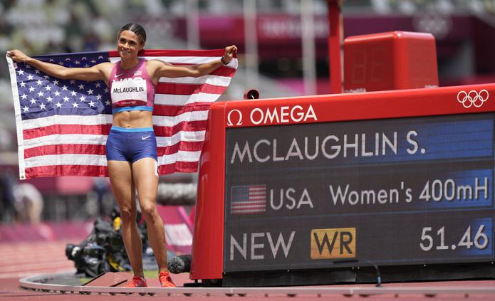 La estadounidense Sydney Mclaughlin posa junto al reloj oficial del Estadio Olímpico que muestra su tiempo en los 400 metros con vallas, evento en que ganó el oro al romper su propio récord mundial.