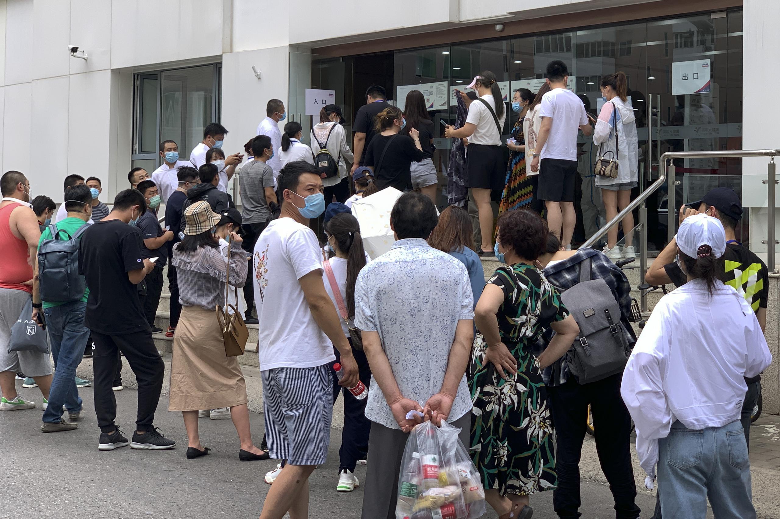 Unas personas con mascarillas se forman afuera de un centro de salud para realizarse una prueba de ácido nucleico en Beijing