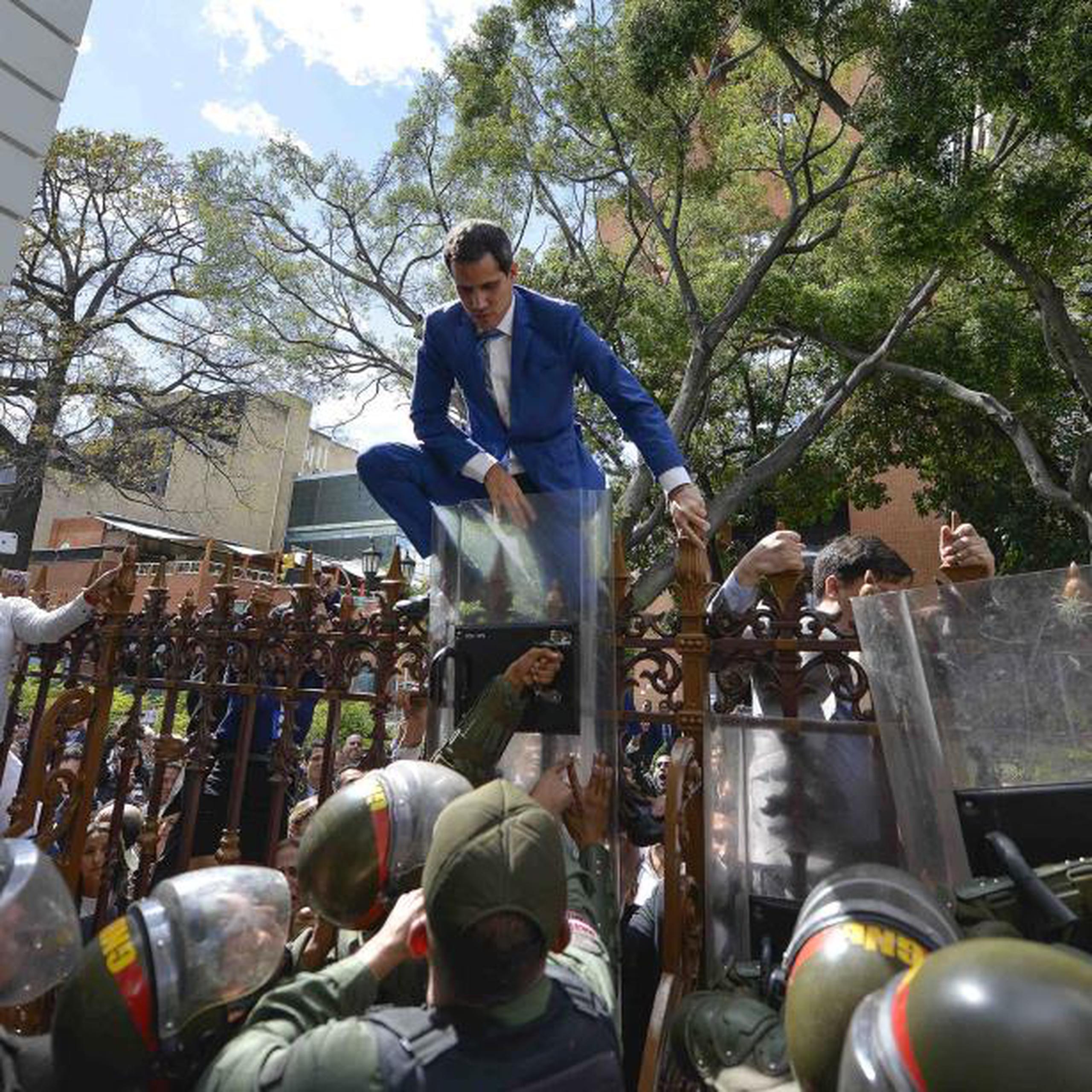 National Assembly President Juan Guaido, Venezuela's opposition leader, tries to climb the fence to enter the compound of the Assembly, after he and other opposition lawmakers were blocked by police from entering a session to elect new Assembly leadership in Caracas, Venezuela, Sunday, Jan. 5, 2020. With Guaido stuck outside, a rival slate headed by lawmaker Luis Parra swore themselves in as leaders of the single-chamber legislature. (AP Photo/Matias Delacroix)