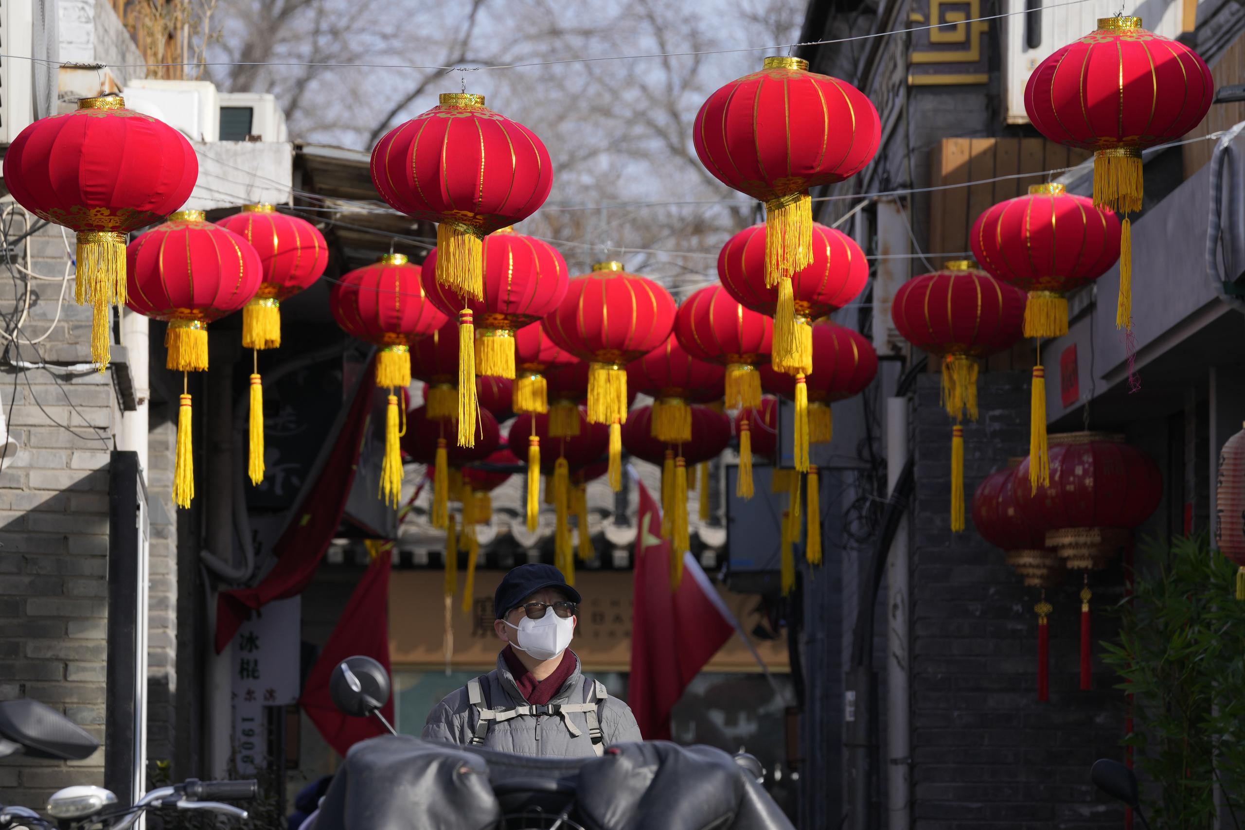 Una persona con mascarilla camina bajo faroles rojos colocados por el Año Nuevo Lunar en Beijing, China.