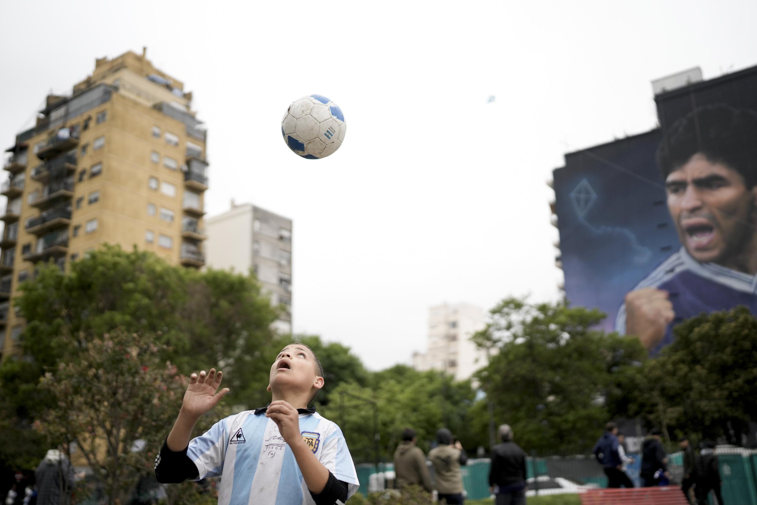 Un niño juega con un balón frente a un mural de Diego Maradona del artista Martín Ron en Buenos Aires, Argentina, el domingo 30 de octubre de 2022. (AP Foto/Rodrigo Abd)