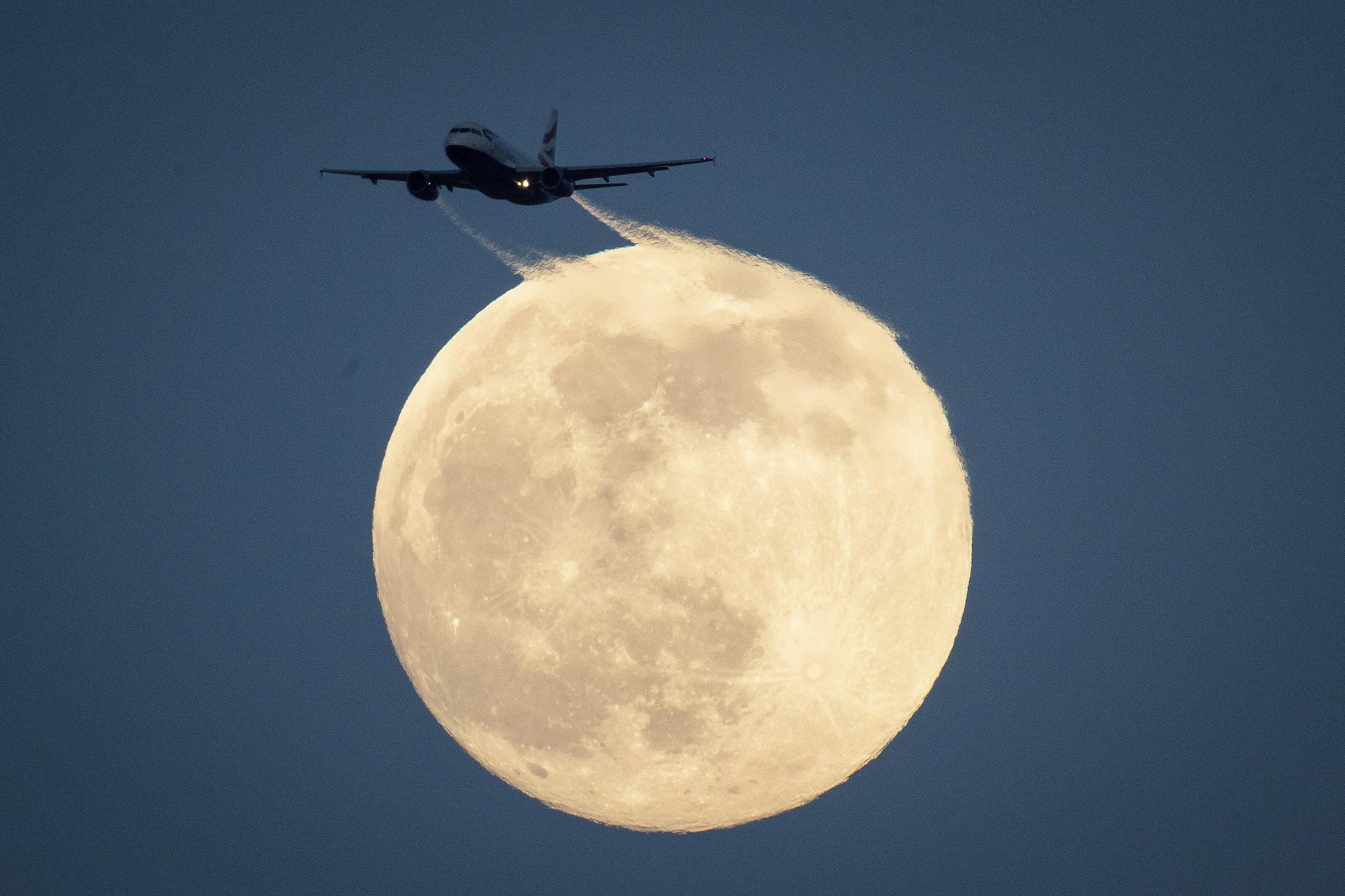 Un avión vuela delante de la Luna.