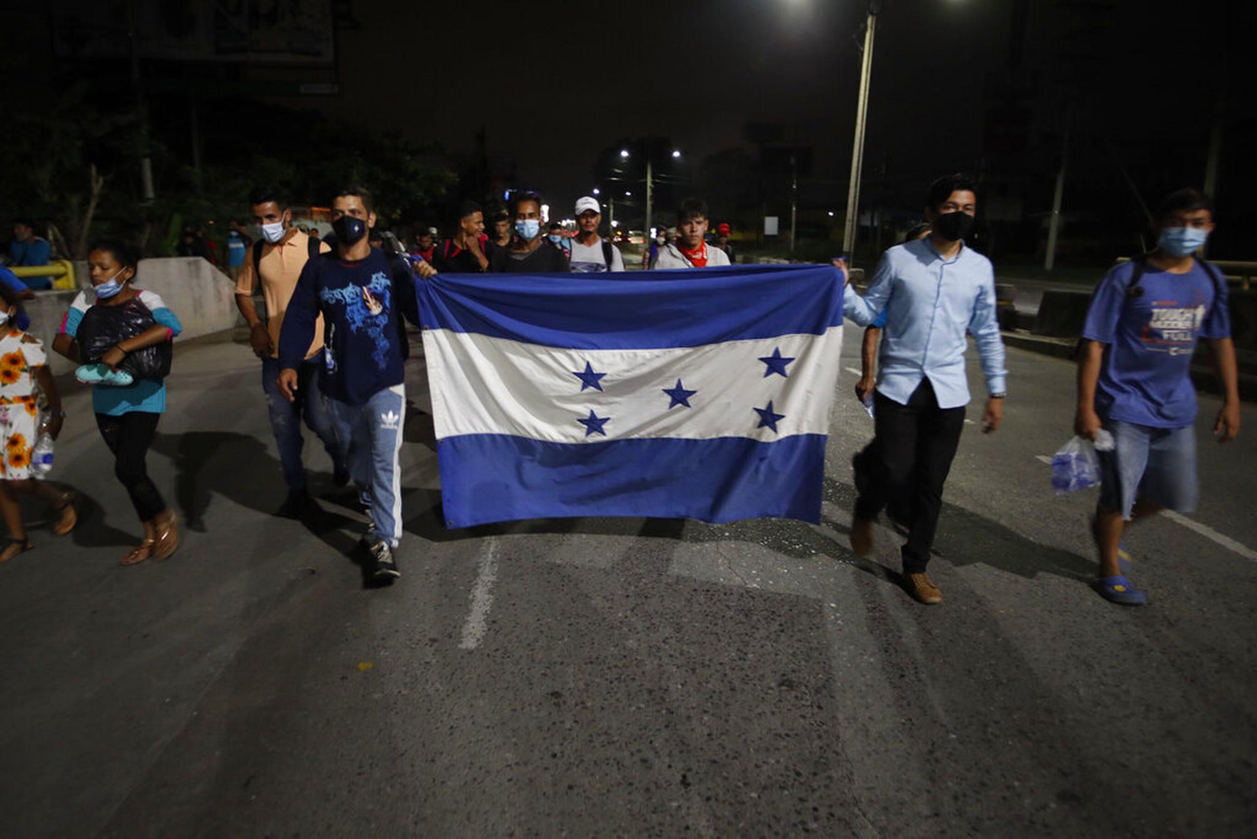 Portando una bandera hondureña, migrantes caminan por una autovía a las afueras de San Pedro Sula, en Honduras.