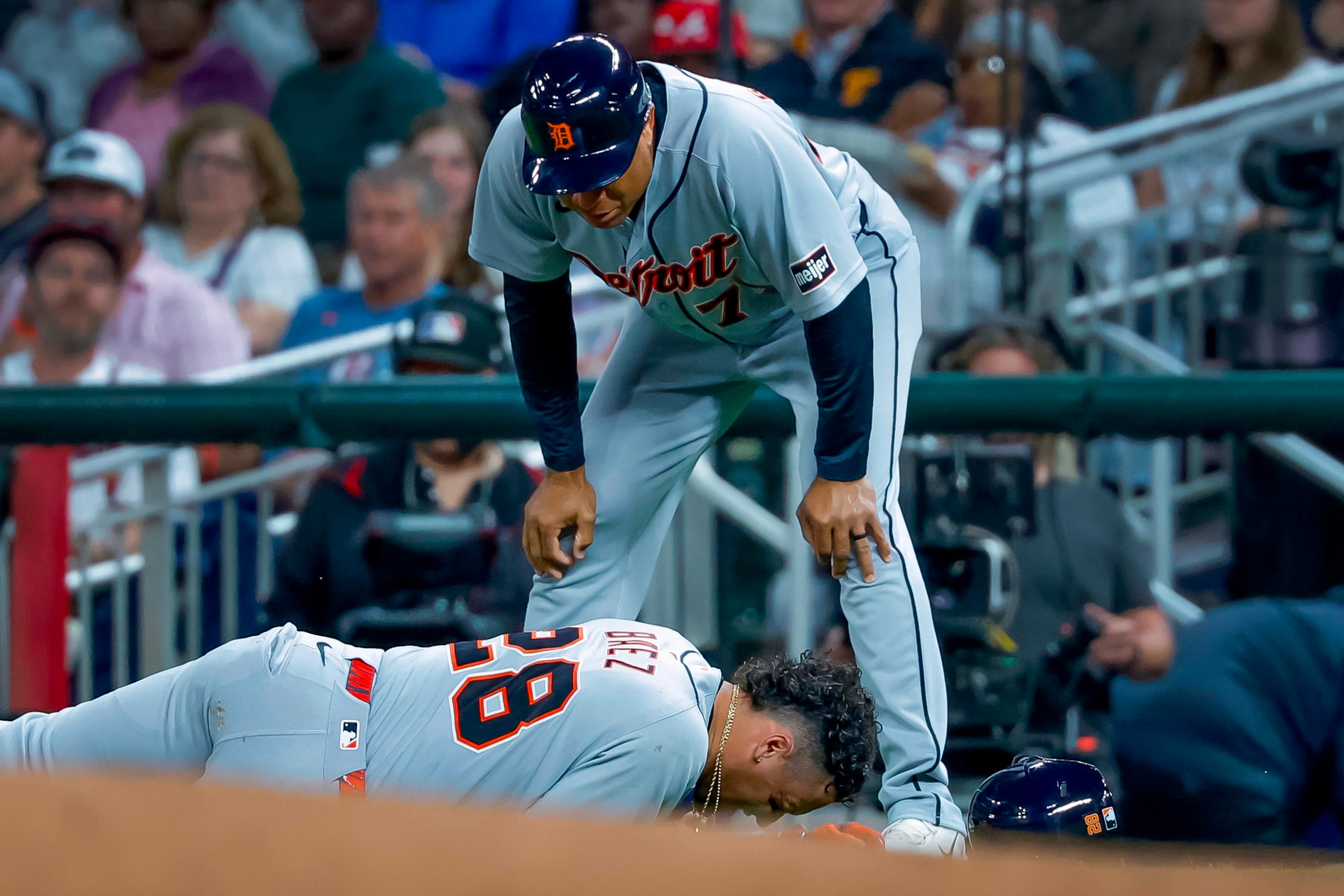 Javier Báez (28), de los Tigres de Detroit, yace sobre el terreno tras lesionarse mientras corría hacia la primera base en el partido frente a los Bravos de Atlanta, mientras el coach de primera base de los Tigres, Anthony Sanders (77), observa. (AP Foto/Erik S. Lesser)