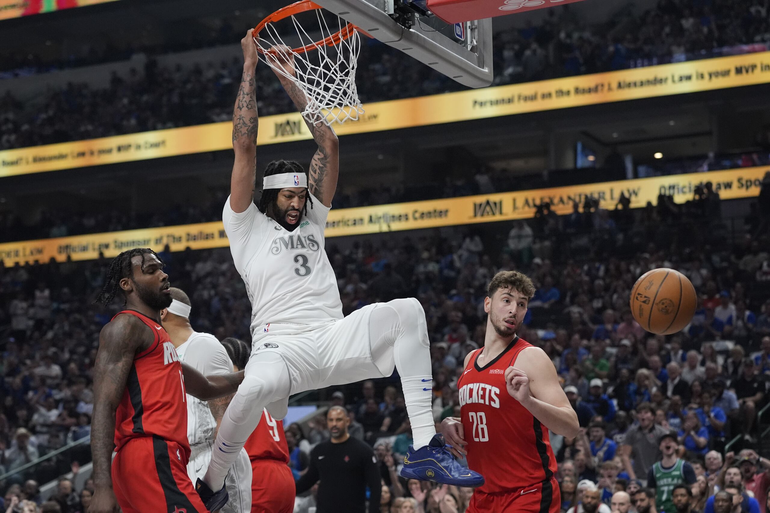 El centro de los Mavericks de Dallas Anthony Davis (3) se cuelga del aro después de clavar sobre el alero de los Rockets de Houston Tari Eason (17) y el pívot Alperen Sengun (28) durante la primera mitad de un partido de baloncesto de la NBA el sábado 8 de febrero de 2025, en Dallas.