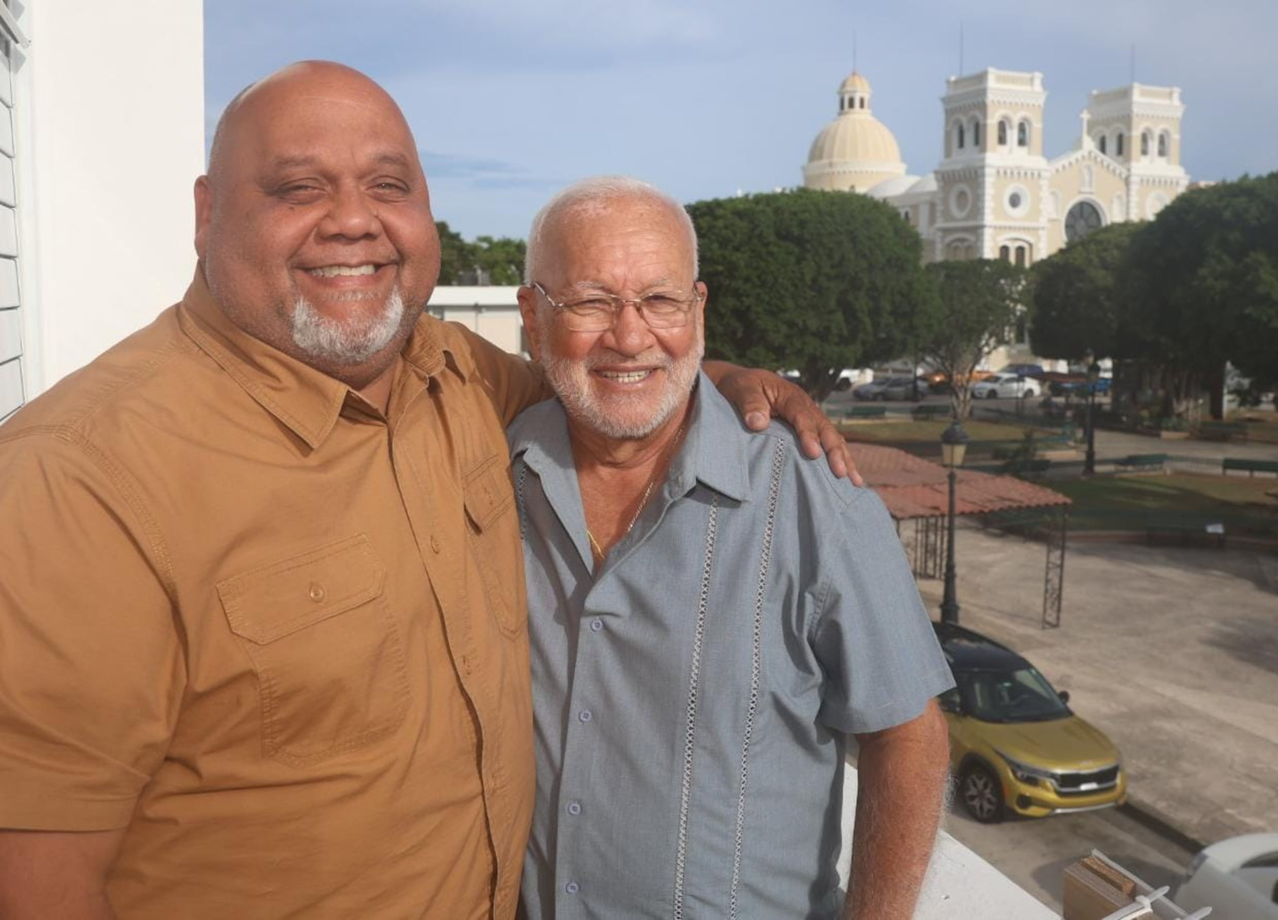 El alcalde de Guayama, O'brian Vázquez, posa junto al cantante Chamaco Rivera con la plaza Cristóbal Colón de fondo.