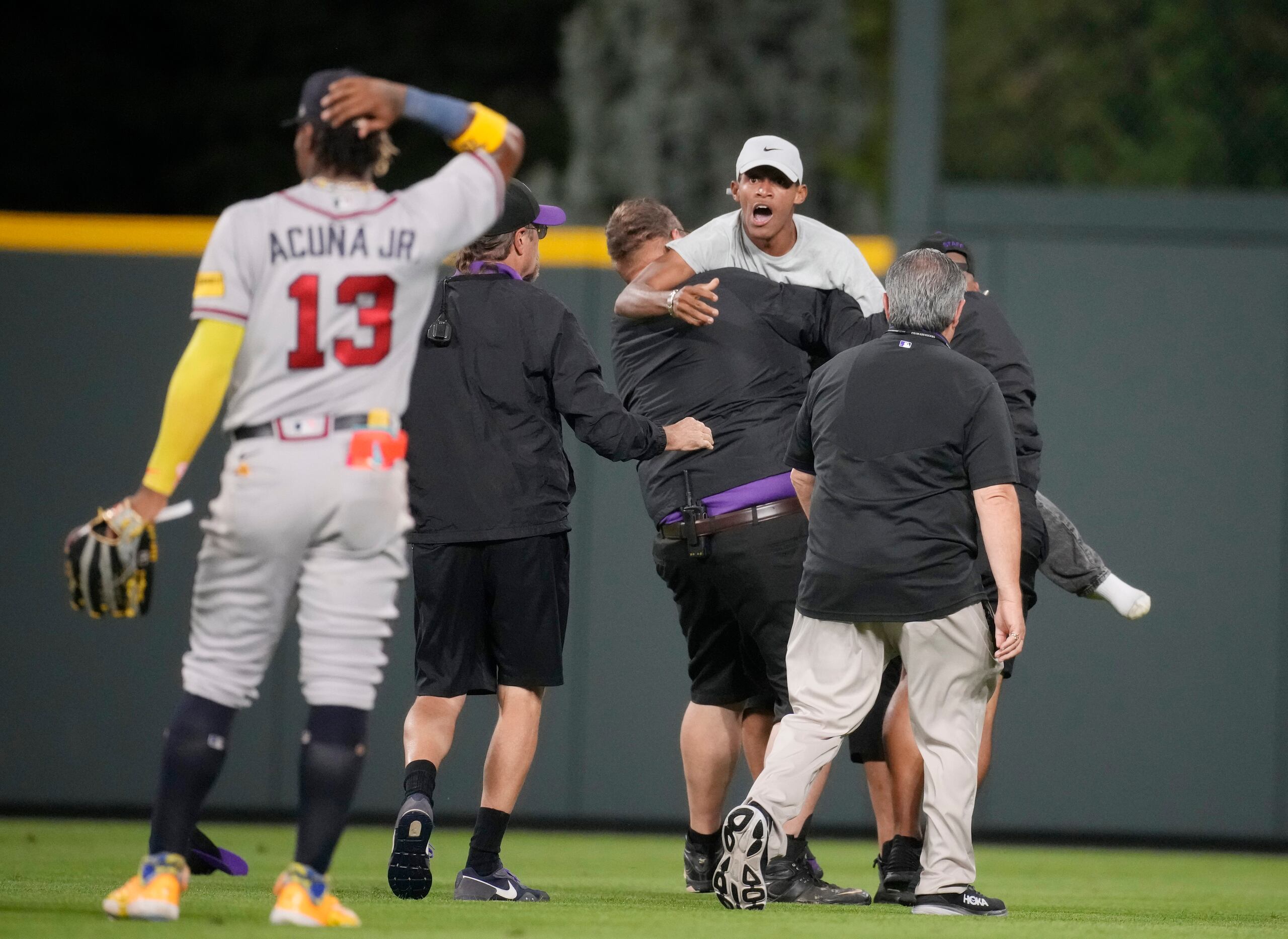 La seguridad saca del terreno a dos aficionados que se acercaron a Ronald Acuña Jr., jardinero derecho de los Bravos de Atlanta, en el juego ante los Rockies de Colorado ayer en Colorado.
