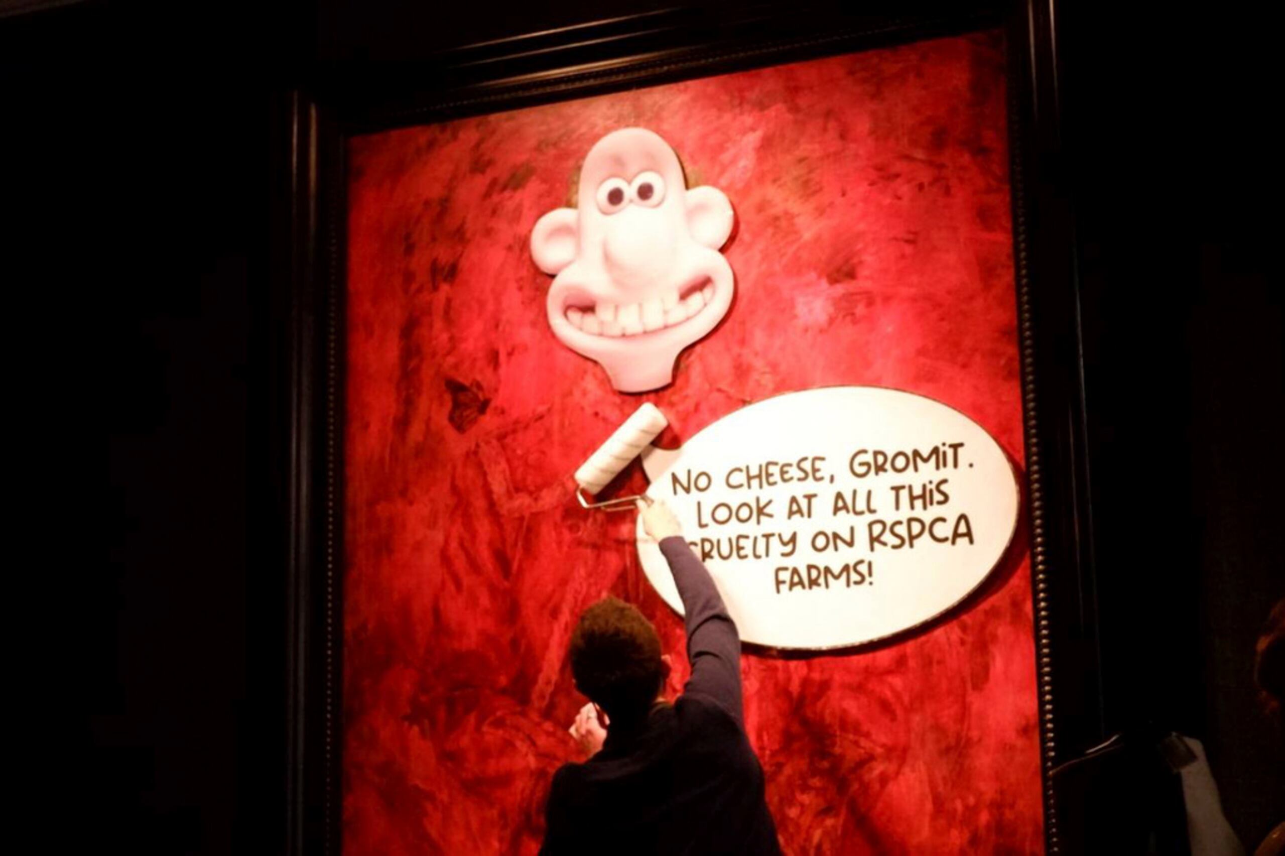 En un globo de diálogo junto a la cabeza de Wallace se lee: “No hay queso, Gromit. ¡Mira toda esta crueldad en las granjas de la RSPCA!”.