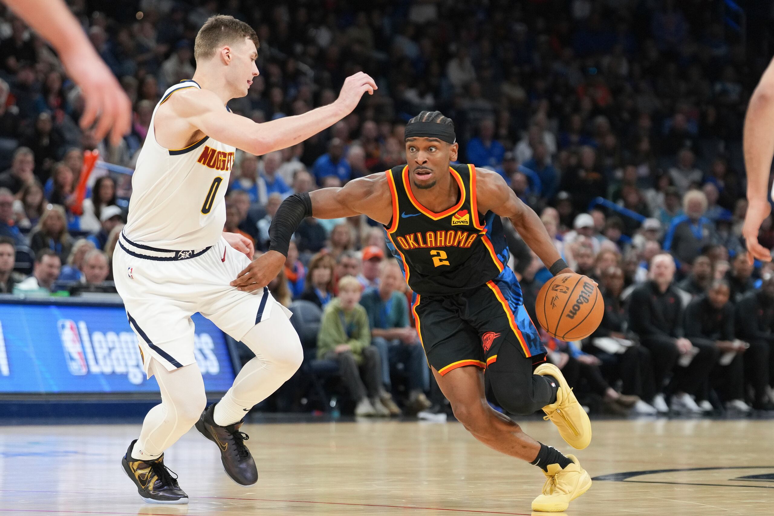 El escolta del Thunder de Oklahoma City, Shai Gilgeous-Alexander (2), supera al escolta de los Nuggets de Denver, Christian Braun (0), durante la segunda mitad de un partido de baloncesto de la NBA, el domingo 9 de marzo de 2025, en Oklahoma City. (AP Foto/Kyle Phillips)