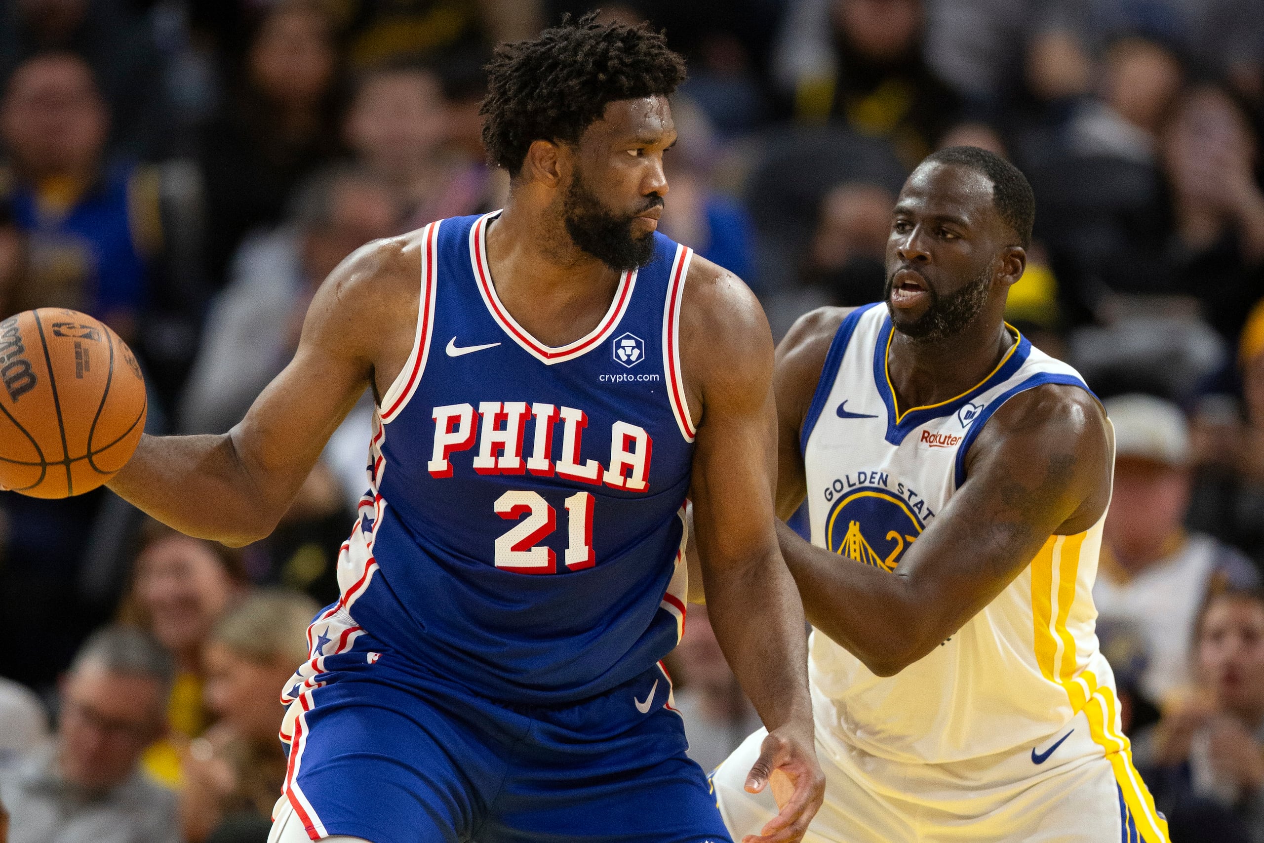 El pívot de los 76ers de Filadelfia Joel Embiid observa antes de pasar el balón mientras lo defiende el alero de los Warriors de Golden State Draymond Green en el encuentro del martes 30 de enero del 2024.