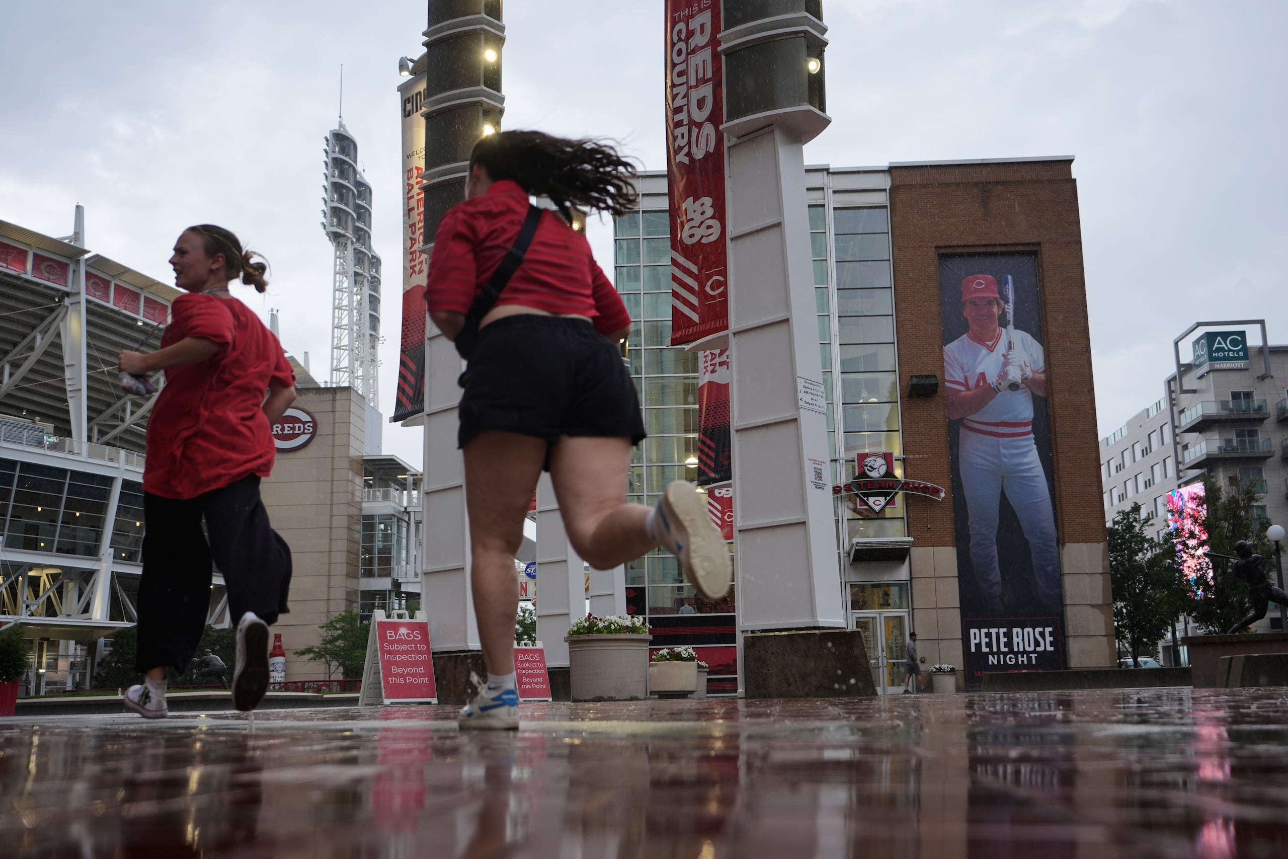 Aficionados buscan refugio de la lluvia frente a una pancarta de Pete Rose, ex pelotero de los Rojos de Cincinnati, afuera del estadio Great American Ball Park, el martes 13 de mayo de 2025, Cincinnati. (AP Foto/Carolyn Kaster)