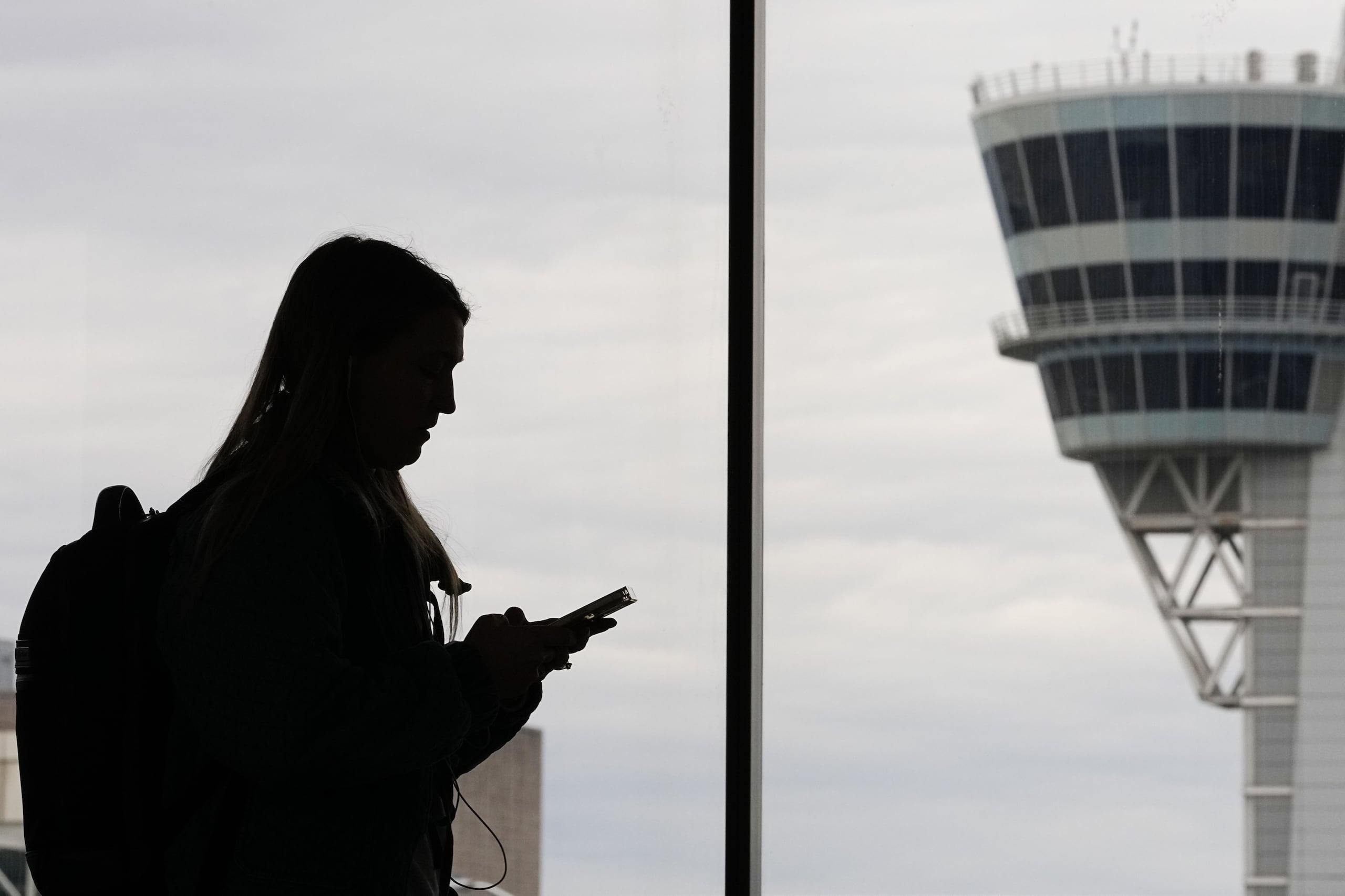 ARCHIVO – Una viajera con un teléfono inteligente camina frente a una torre de control de tráfico aéreo en el Aeropuerto Internacional de Filadelfia, en Filadelfia, el 27 de marzo de 2026. (AP Foto/Matt Rourke, Archivo)