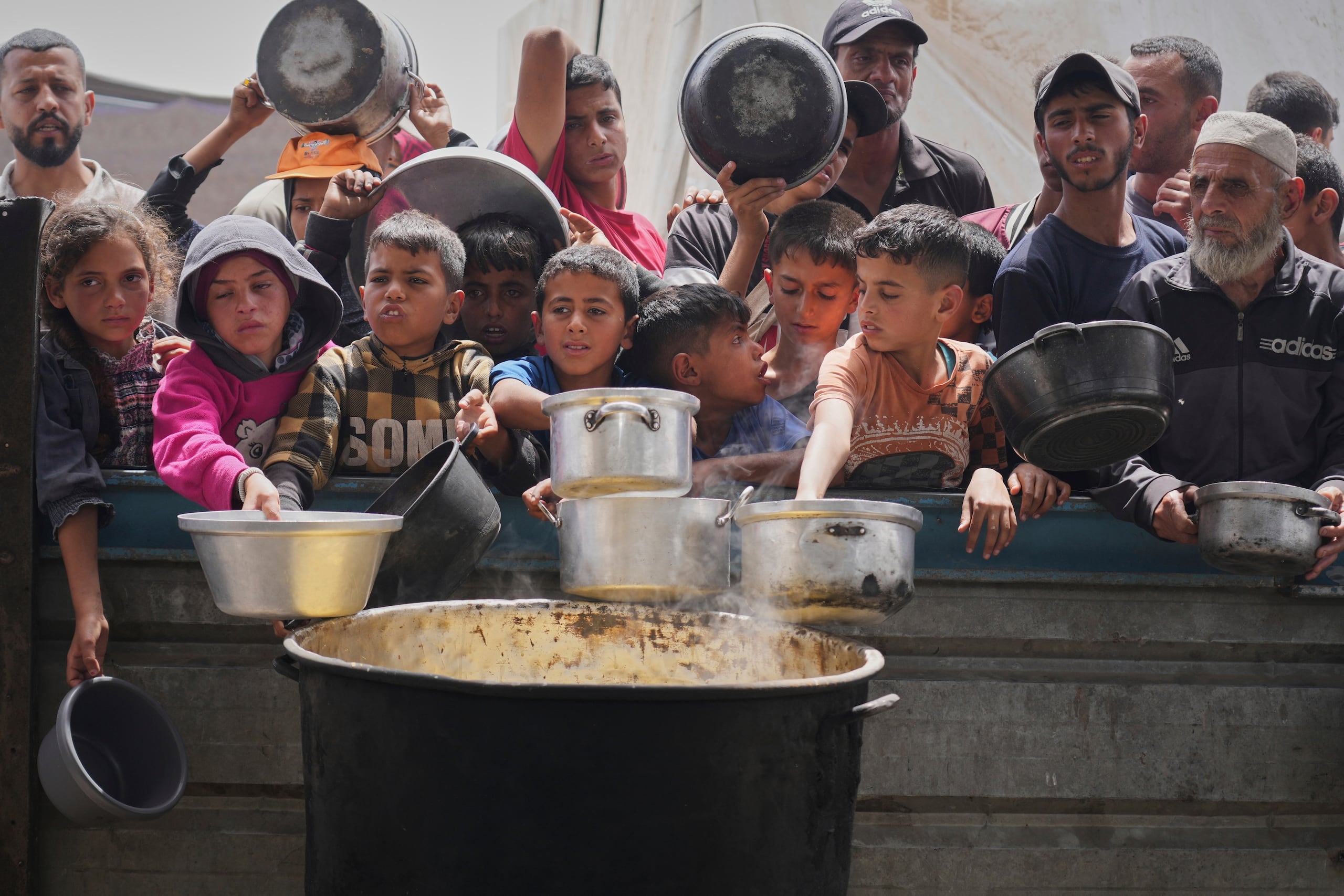 Niños y adultos palestinos esperan para recibir comida en una cocina comunitaria en Jan Yunis, en el sur de la Franja de Gaza, el jueves 24 de abril de 2025. (AP Foto/Abdel Kareem Hana)