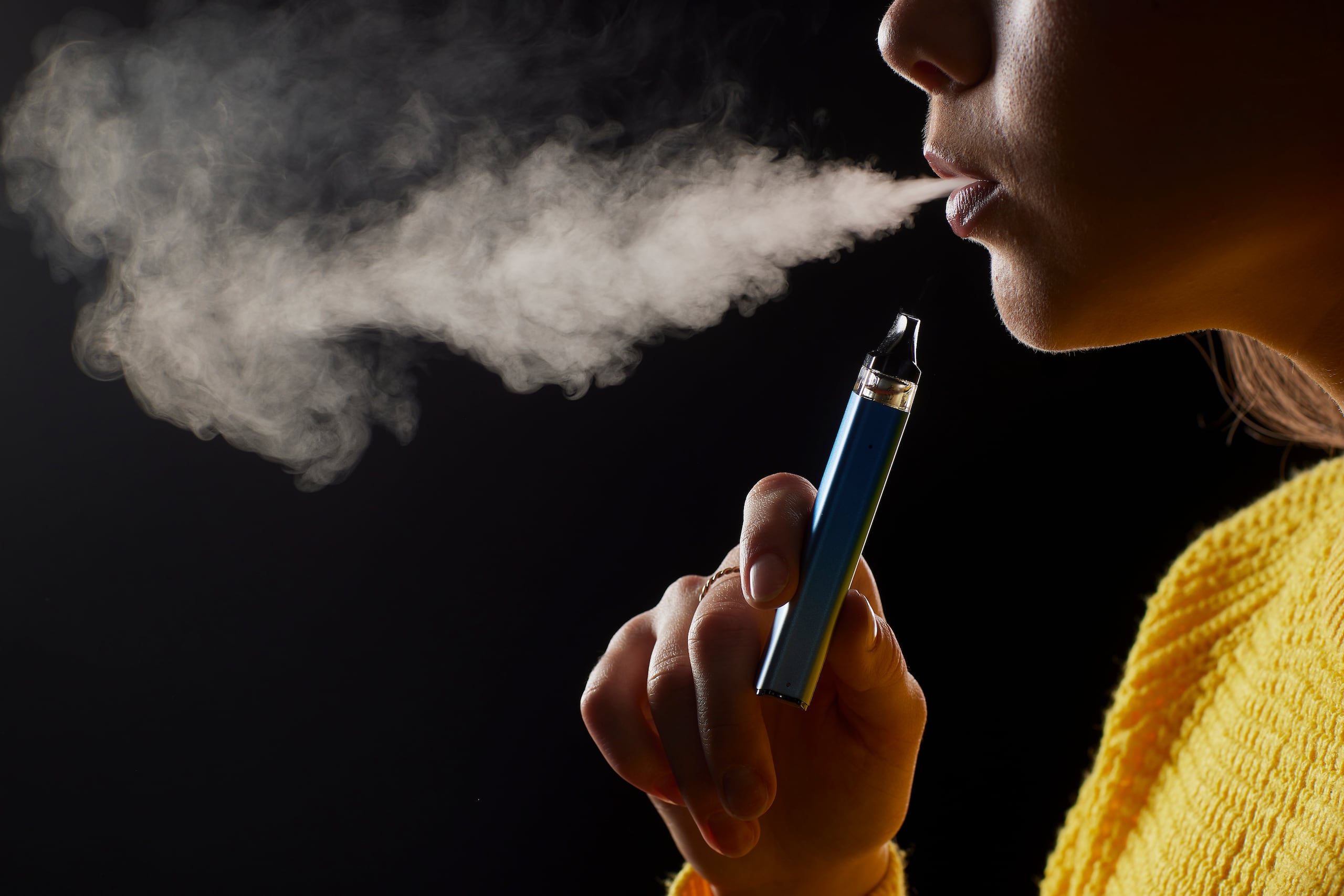 Vapeo, vaping, vape / young girl smokes a vape close-up on a dark background