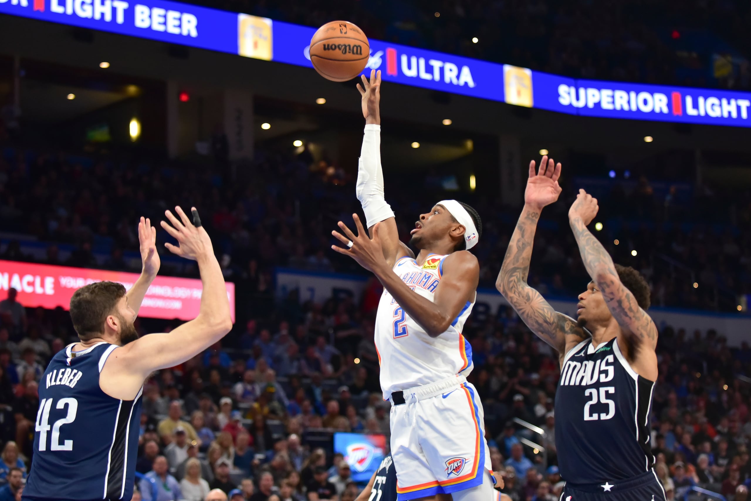 El base del Thunder de Oklahoma City, Shai Gilgeous-Alexander, lanza el balón entre los aleros de los Mavericks de Dallas, Maxi Kleber y P.J. Washington.