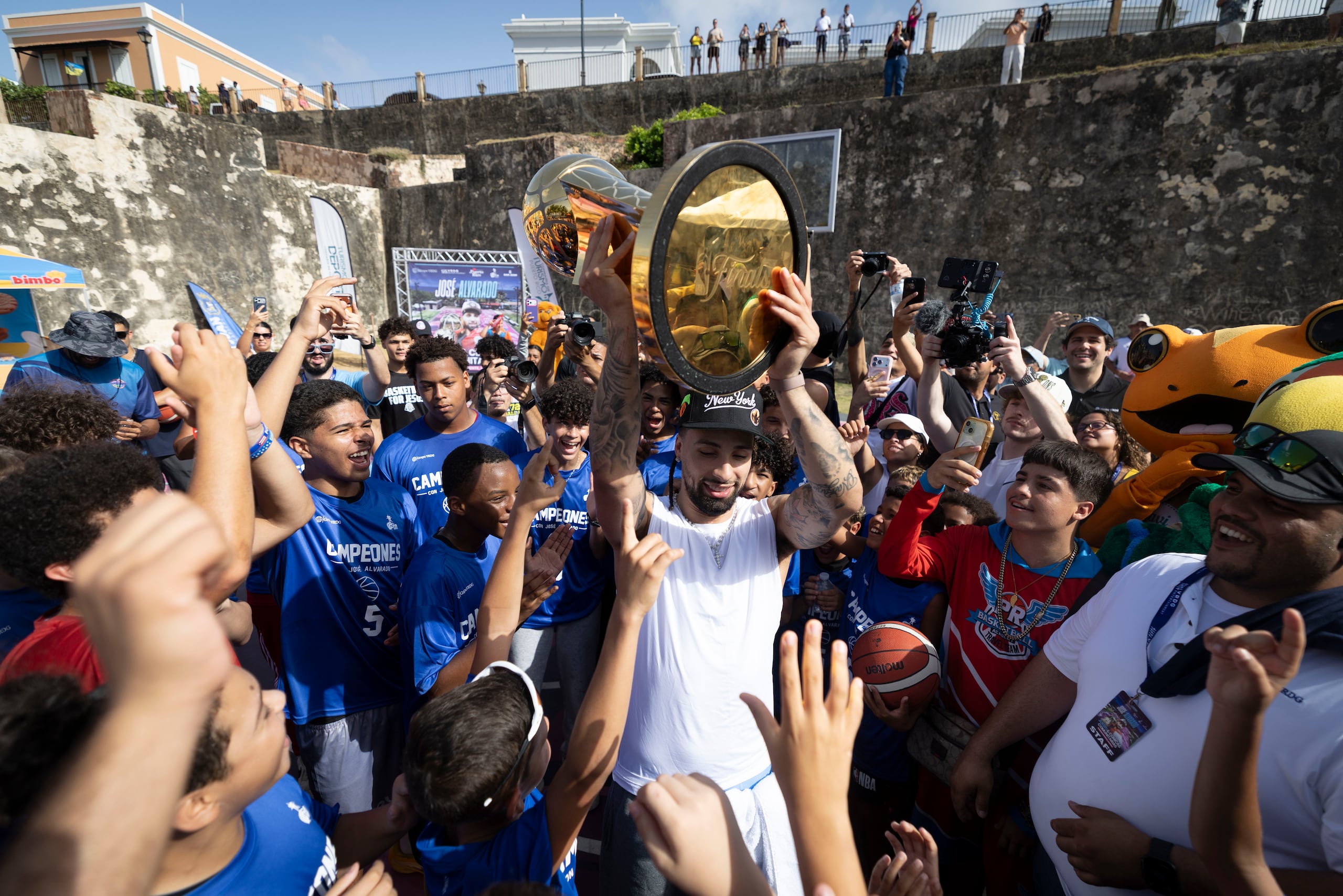 José Alvarado sostiene el trofeo Larry O’Brien rodeado de jóvenes en la cancha de La Perla.