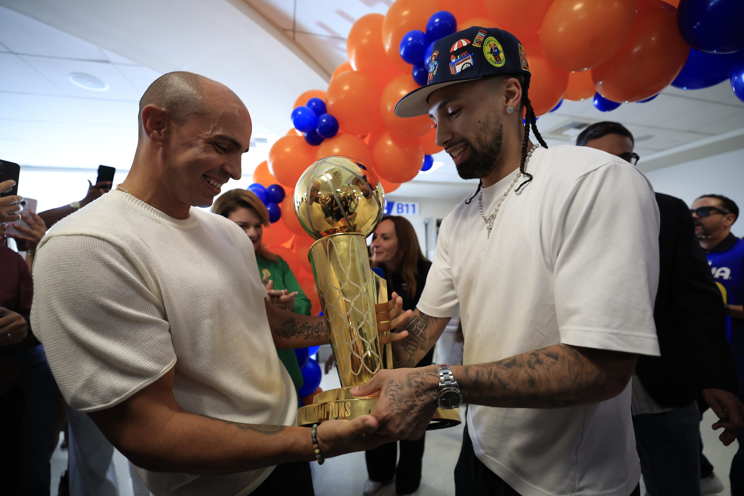José Alvarado y Carlos Arroyo sostienen el trofeo Larry O'Brien en el Aeropuerto Internacional Luis Muñoz Marín.