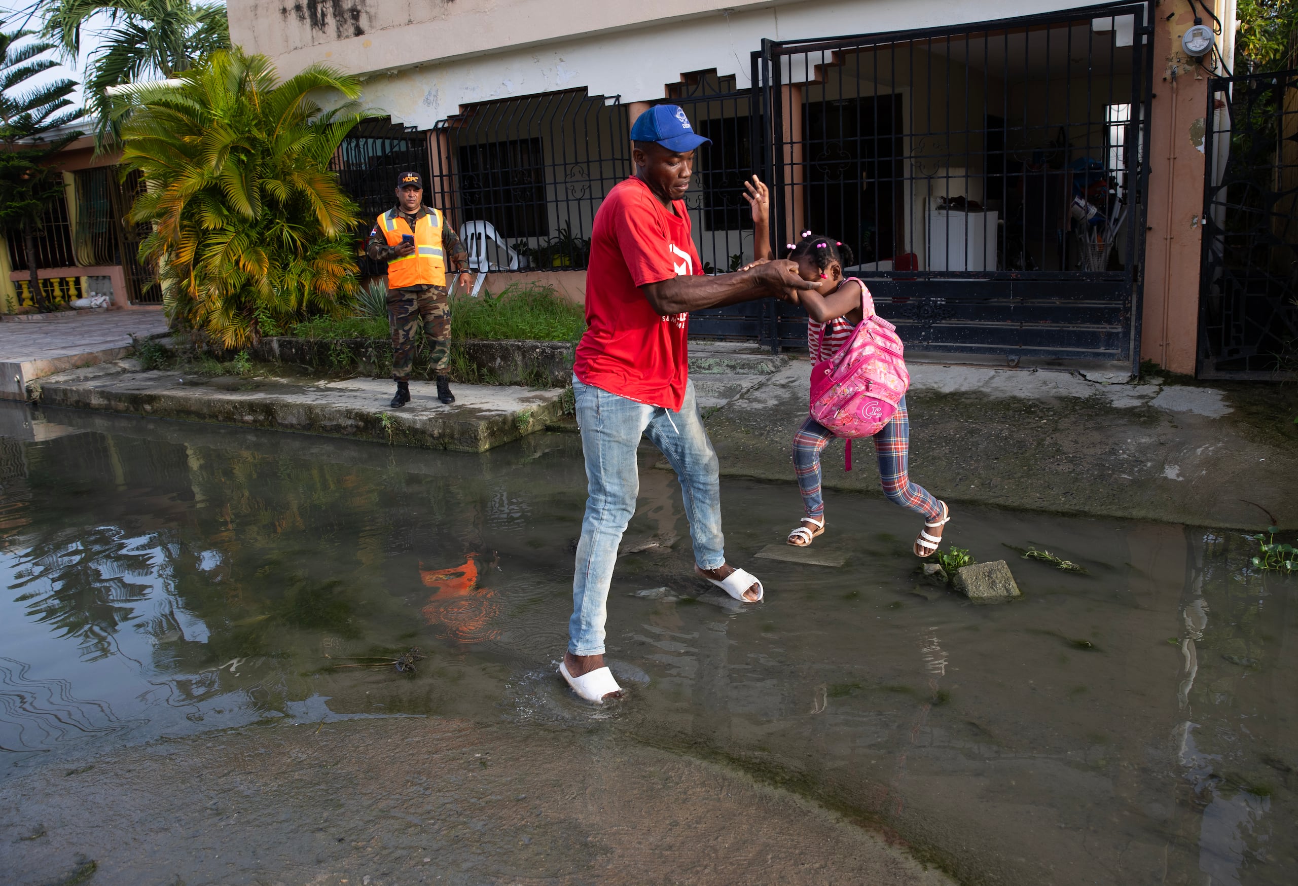 Un hombre y una niña cruzan una calle inundada durante una jornada de fumigación por parte de la Comisión Militar y Policial para eliminar criaderos del mosquito transmisor del dengue en Santo Domingo, en República Dominicana. (EFE/ Orlando Barría)