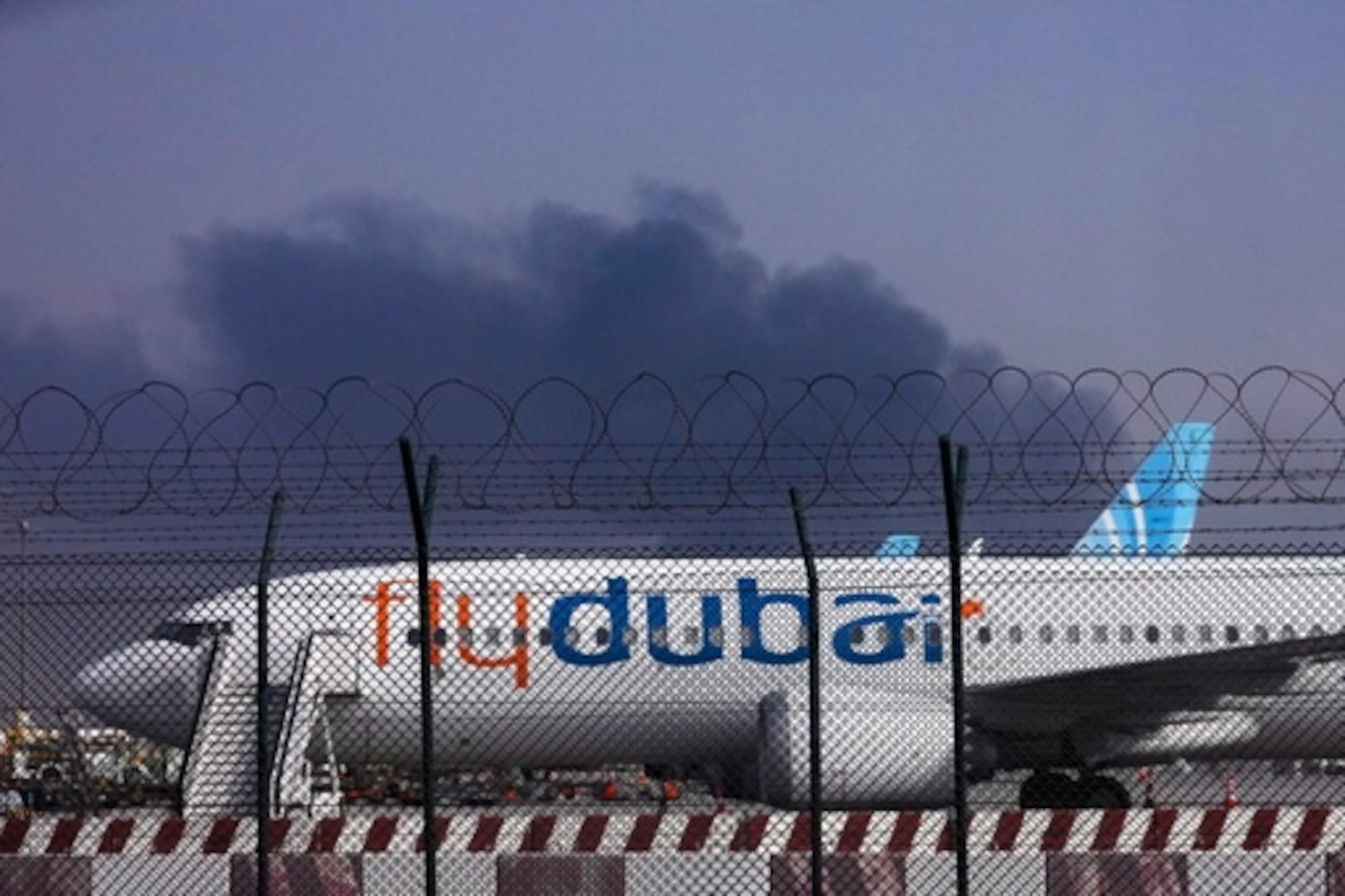 Un avión de FlyDubai está aparcado en el Aeropuerto Internacional de Dubai mientras se levanta humo en el fondo después de que un avión no tripulado golpeara un tanque de combustible a primera hora de la mañana, obligando a la suspensión temporal de los vuelos, en Dubai, Emiratos Árabes Unidos, el lunes 16 de marzo de 2026. (Foto AP)