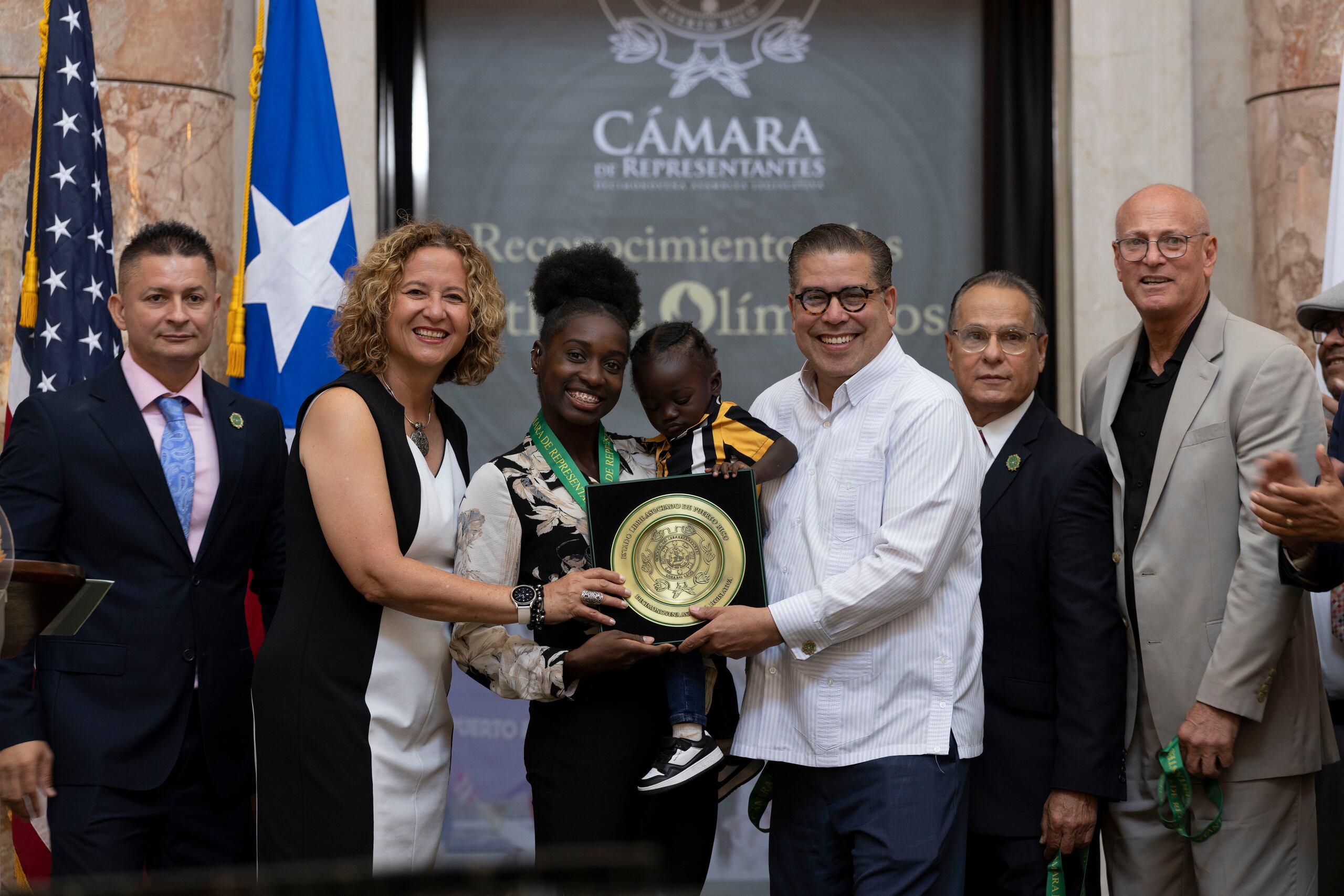 La atleta Grace Claxton, junto a su hijo, también estuvo entre las homenajeadas en la Cámara de Representantes. Desde la izquierda, el representante Eladio 'Layito Cardona, la presidenta del Copur, Sara Rosario, Claxton, su hijo, el presidente de la Cámara, Rafael 'Tatito' Hernánez, y secretario del DRD, Ray Quiñones.