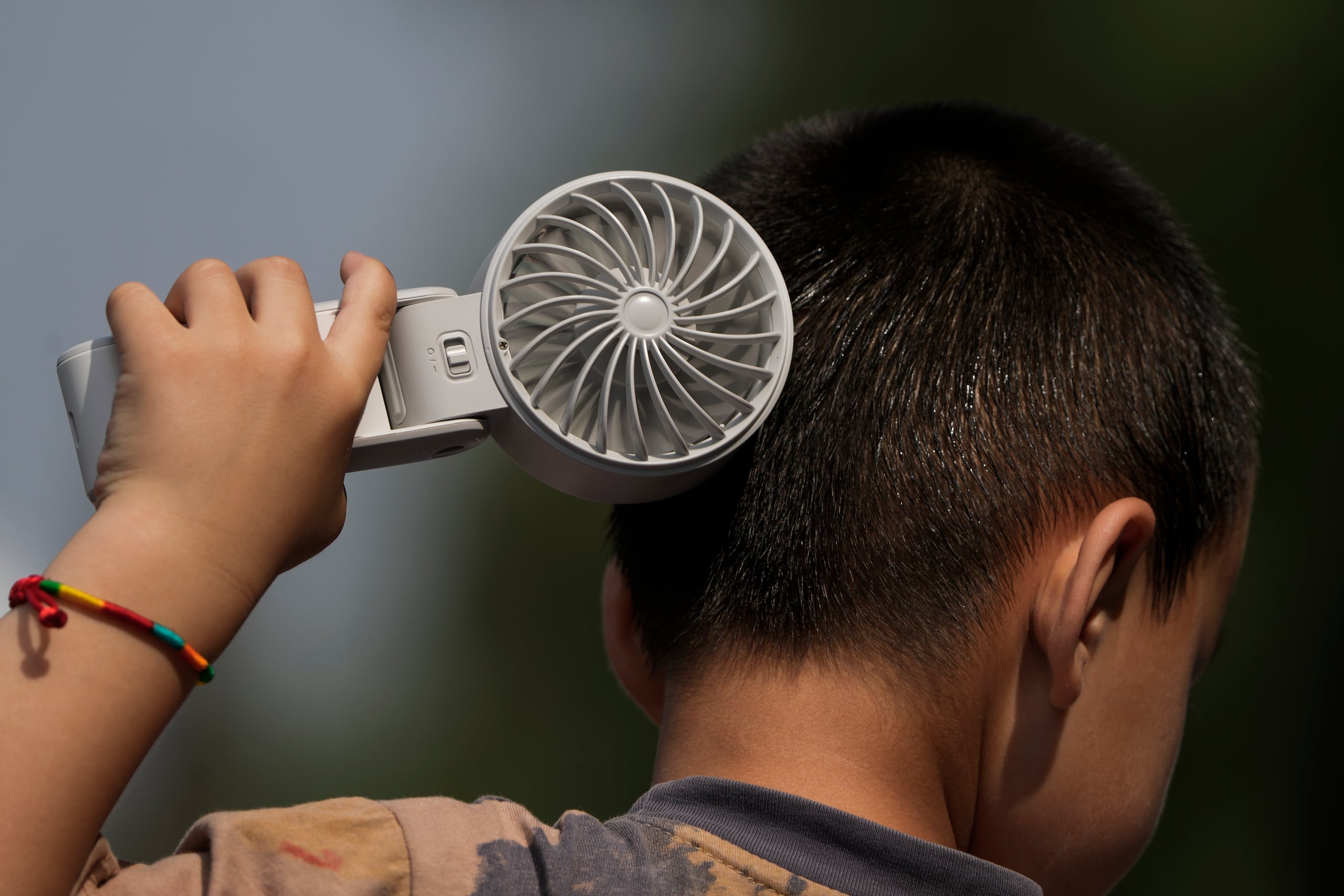 Un niño se refresca con un ventilador eléctrico.