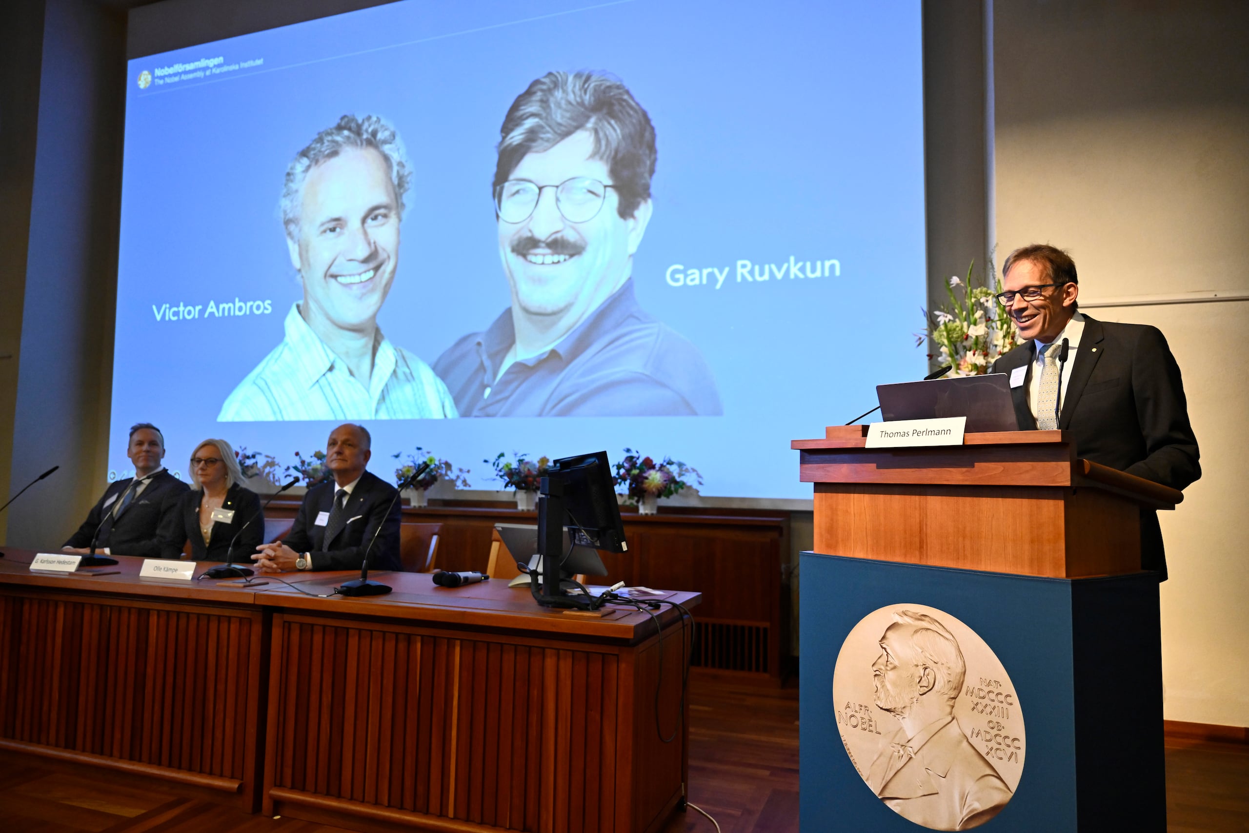 El presidente del Comité del Nobel, Thomas Perlmann, a la derecha, anuncia que los estadounidenses Victor Ambros, a la izquierda, y Gary Ruvkun, mostrados en una pantalla, ganaron el Nobel de Medicina de este año, durante una conferencia de prensa en el Instituto Karolinska de Estocolmo, Suecia.