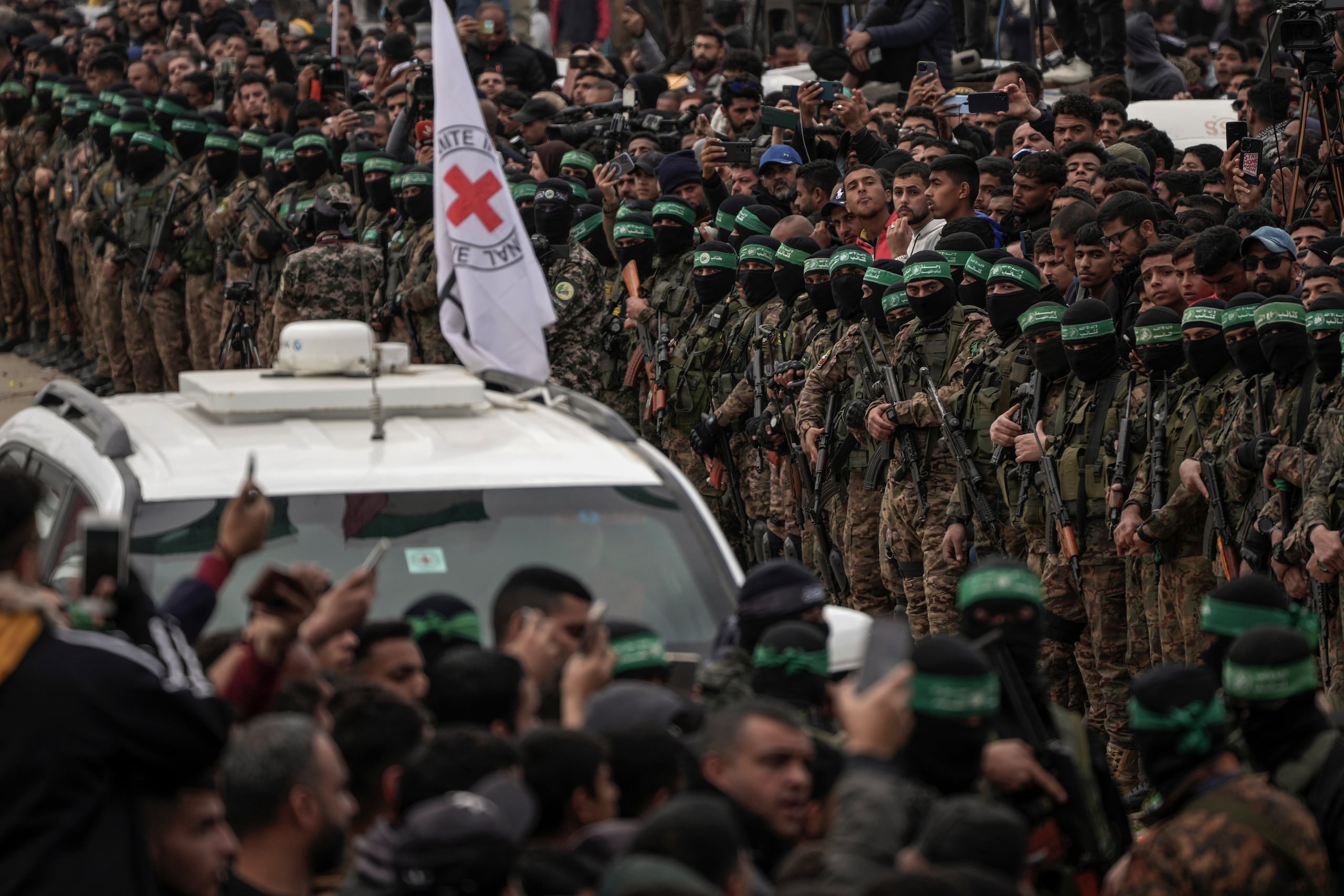 Vehículos de la Cruz Roja esperan mientras combatientes de Hamas se forman antes de la liberación de rehenes en Deir al-Balah, en el centro de la Franja de Gaza, el sábado 8 de febrero de 2025. (Foto AP/Abdel Kareem Hana)