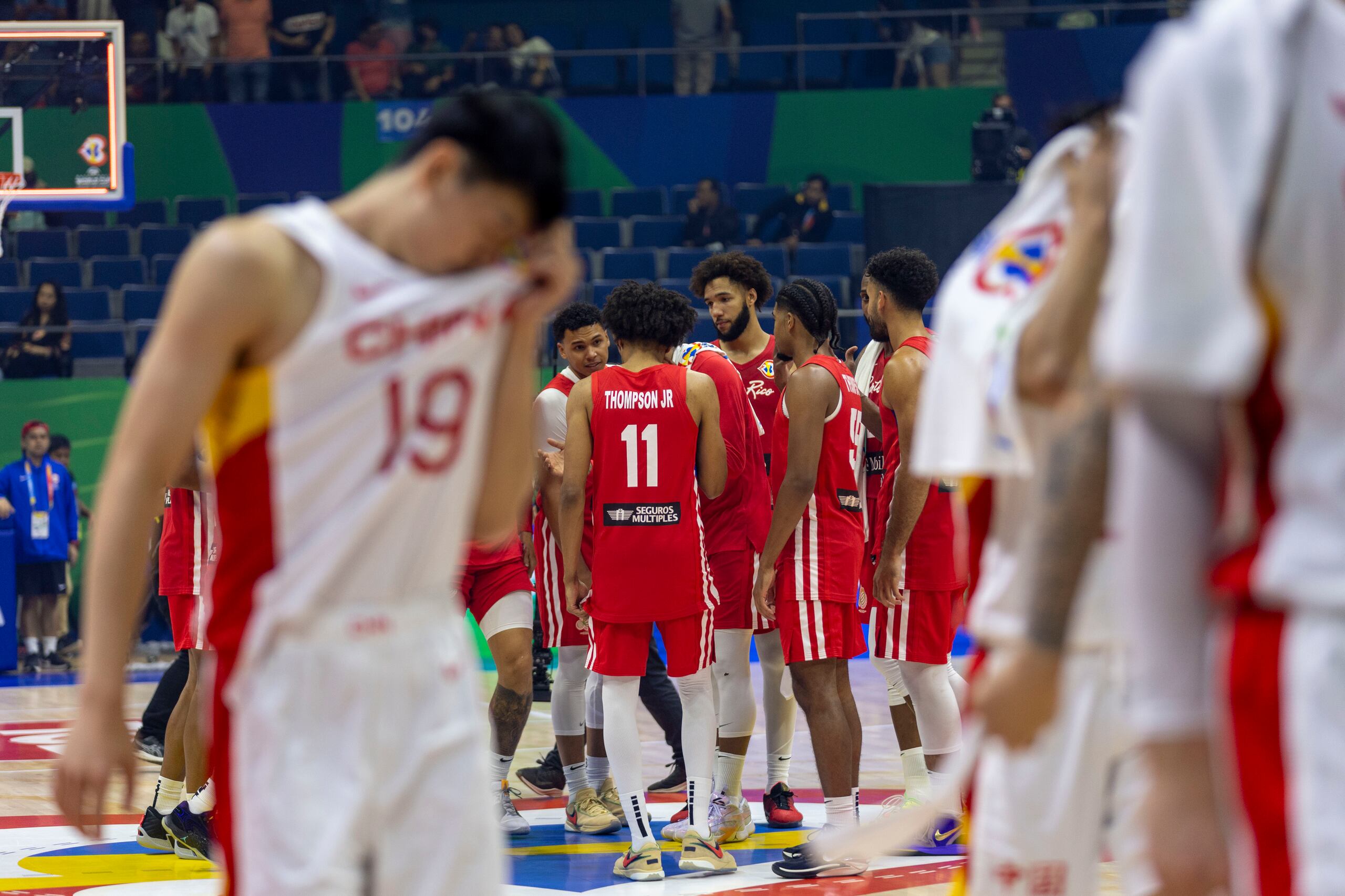 Mientras Puerto Rico celebra al fondo, se ven a jugadores de China salir de la cancha cabizbajos.