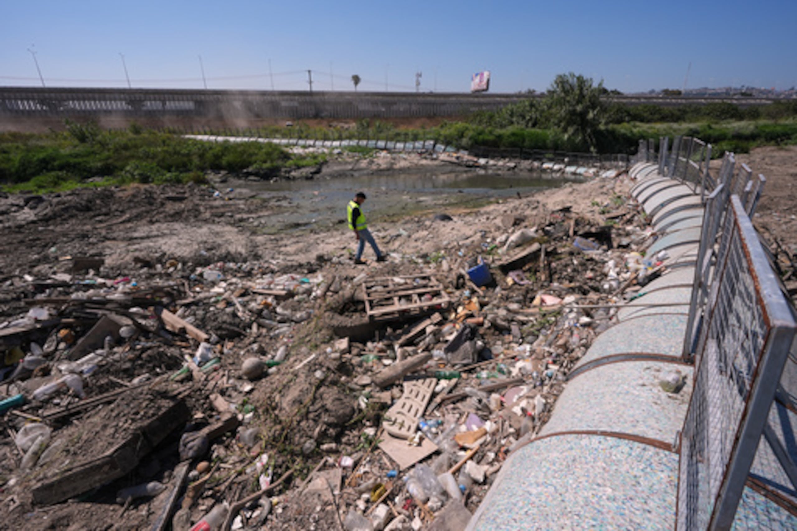 Oscar Romo camina entre los escombros que han sido capturados por una barrera de basura instalada en el río Tijuana en la frontera cerca de donde el río entra en los Estados Unidos desde Tijuana, México, el miércoles 8 de abril de 2026, en San Diego, California (AP Photo/Gregory Bull).